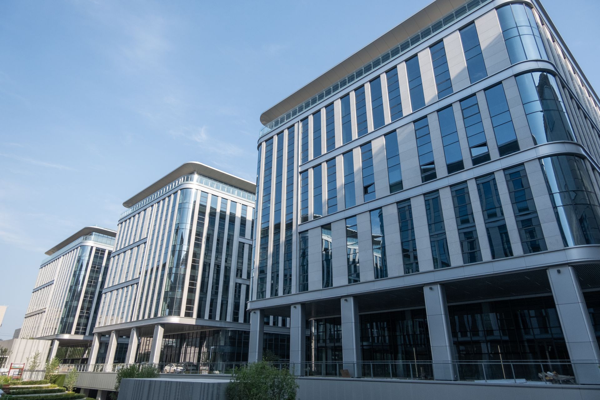 Three modern office buildings with glass-and-steel facades under a clear blue sky.