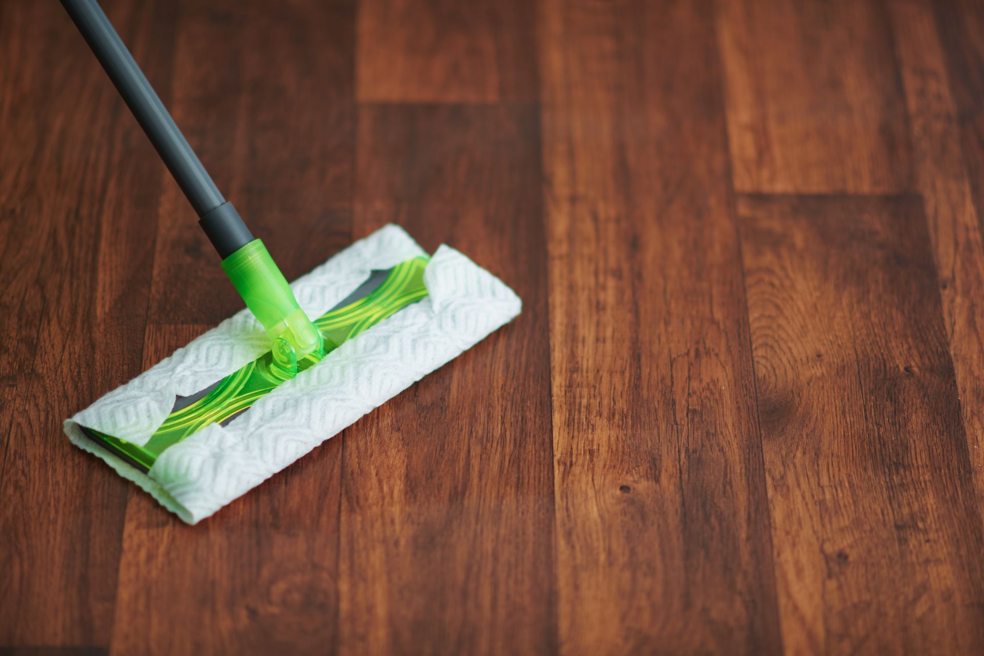 A green and grey mop cleaning a dark brown wood-textured floor.
