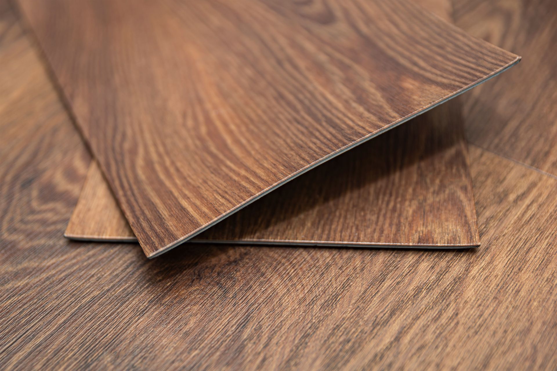 Close-up of brown wood-grain vinyl flooring planks, one partially overlapping the other.