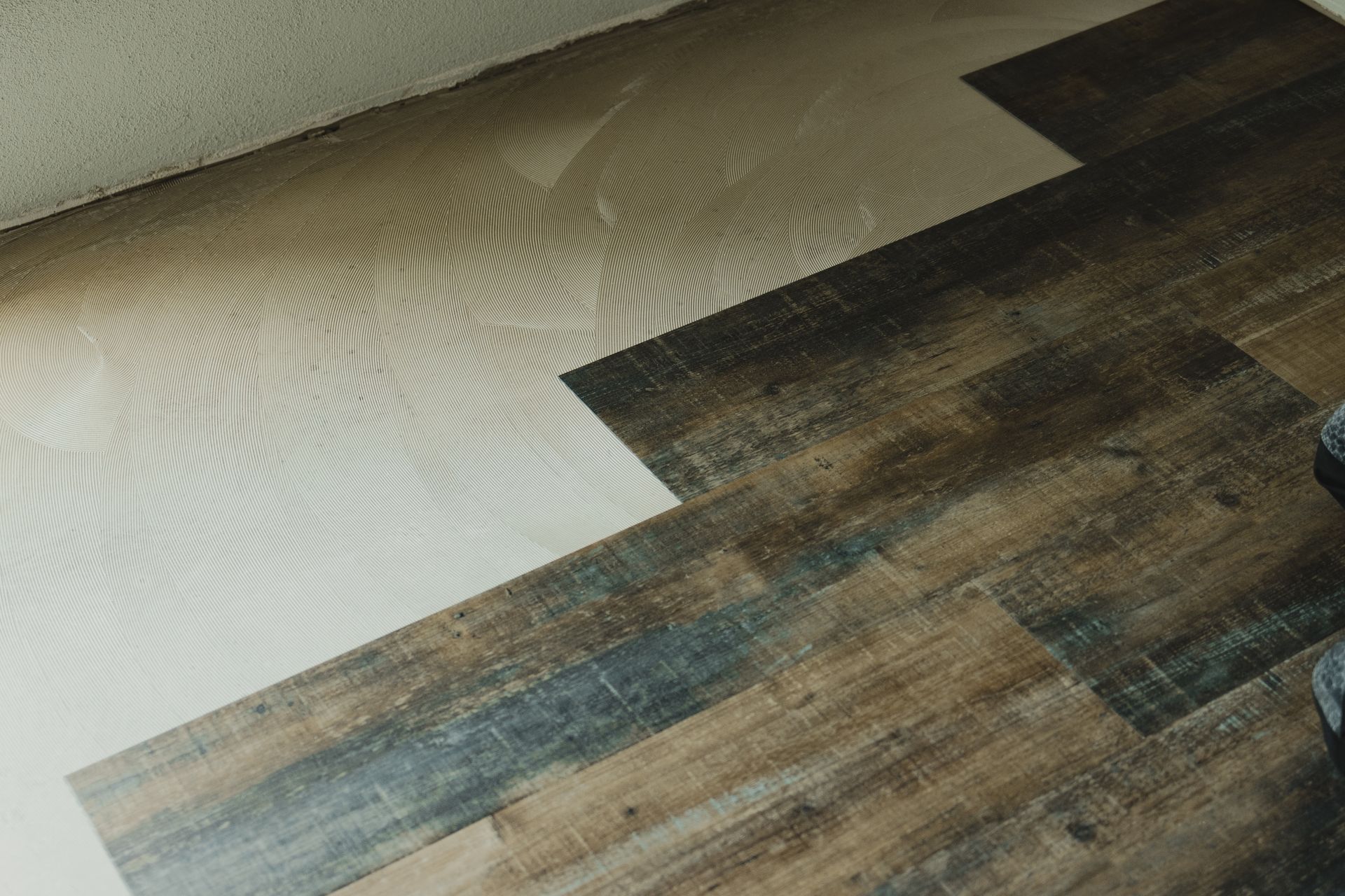 A close-up view of flooring installation showing a contrast between the plain white underlayment and rustic wood planks.