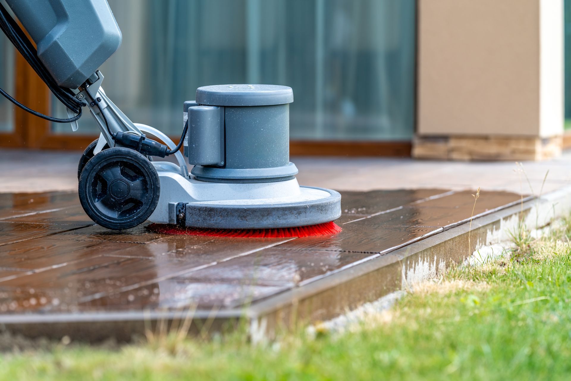 A floor scrubber machine cleans a dark wooden deck next to a grassy lawn.