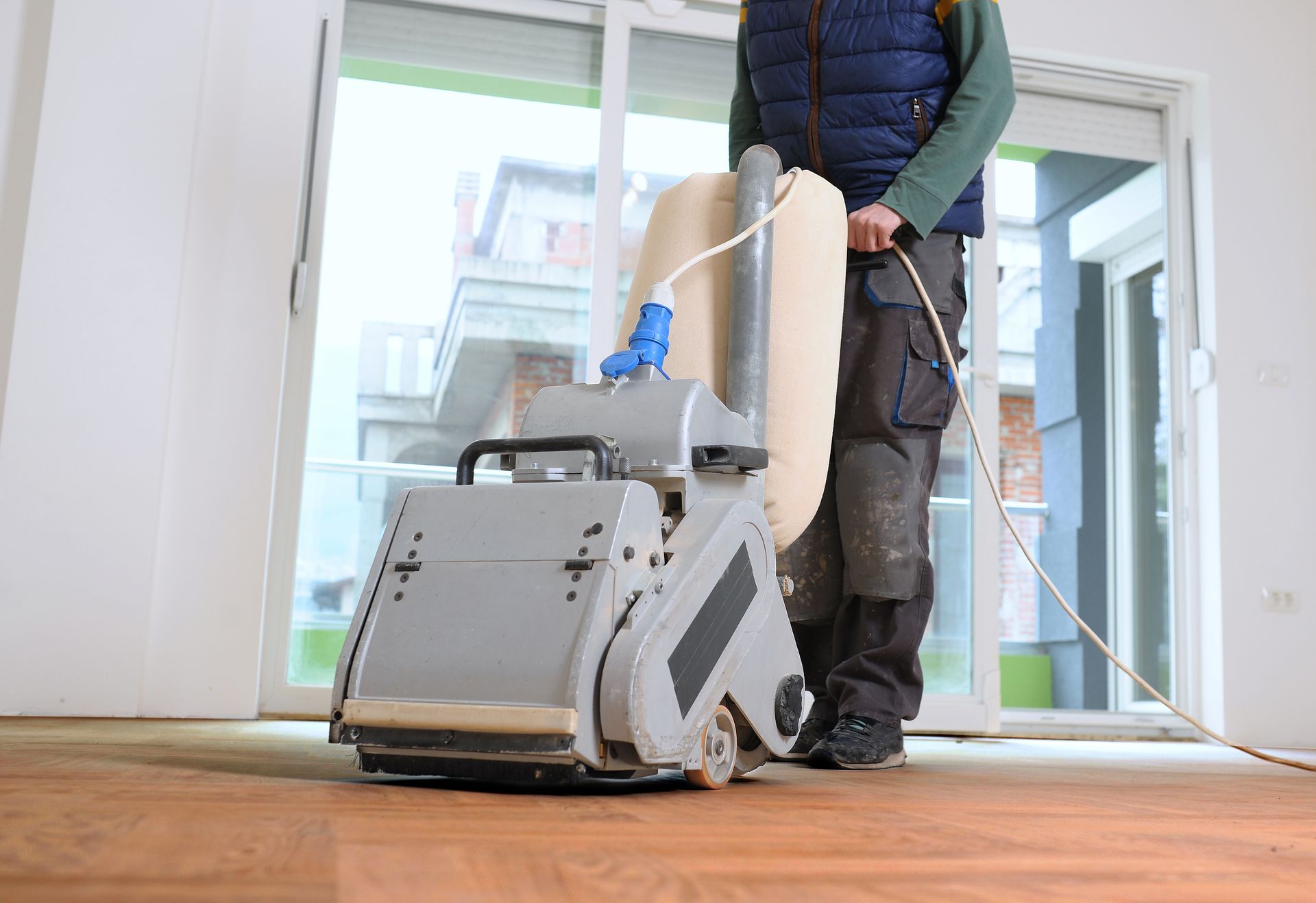 A person uses a floor sanding machine on a wooden parquet floor in a bright, modern room.