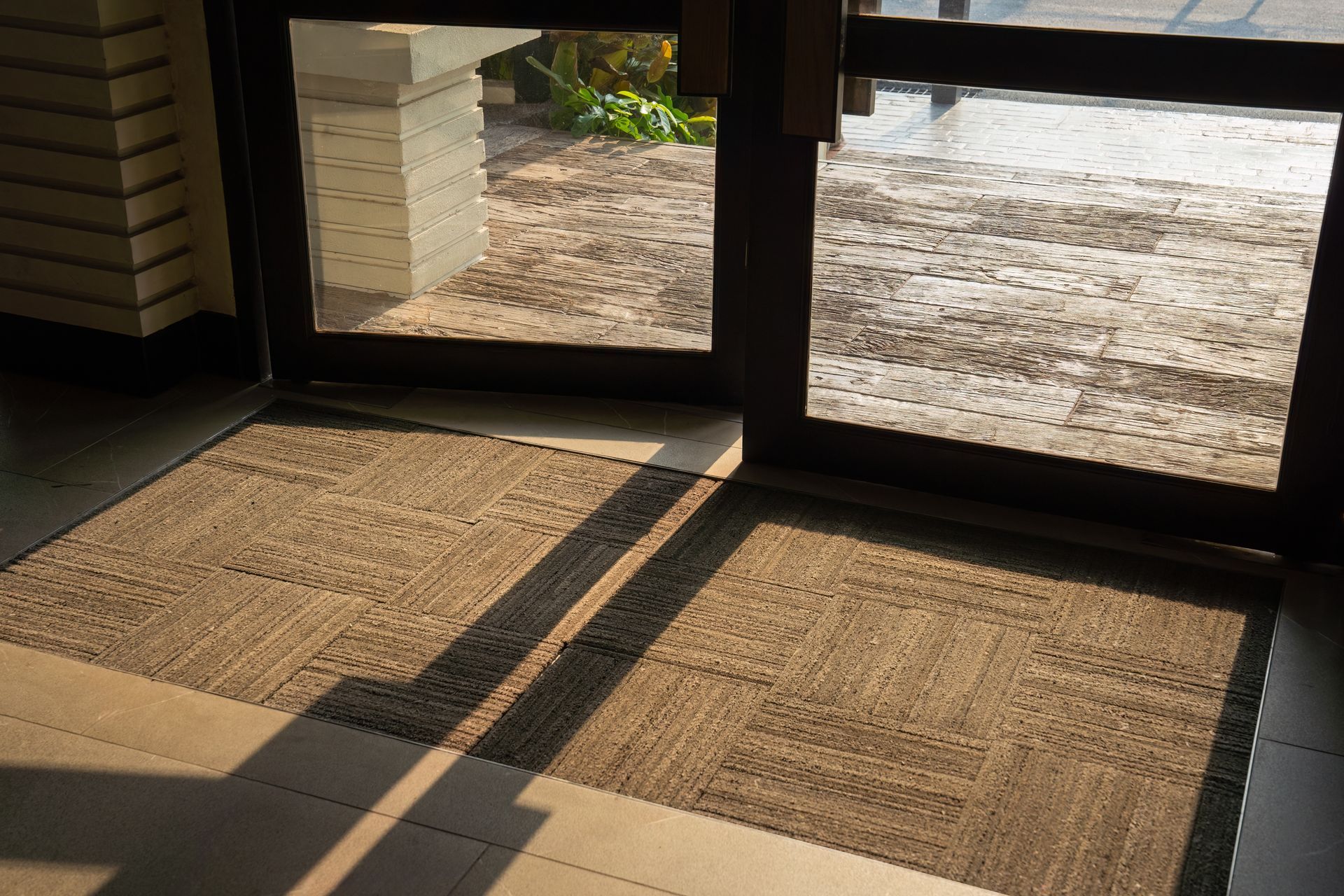 Two rectangular brown floor mats placed side-by-side inside a doorway, with shadows cast across them from the door frame.