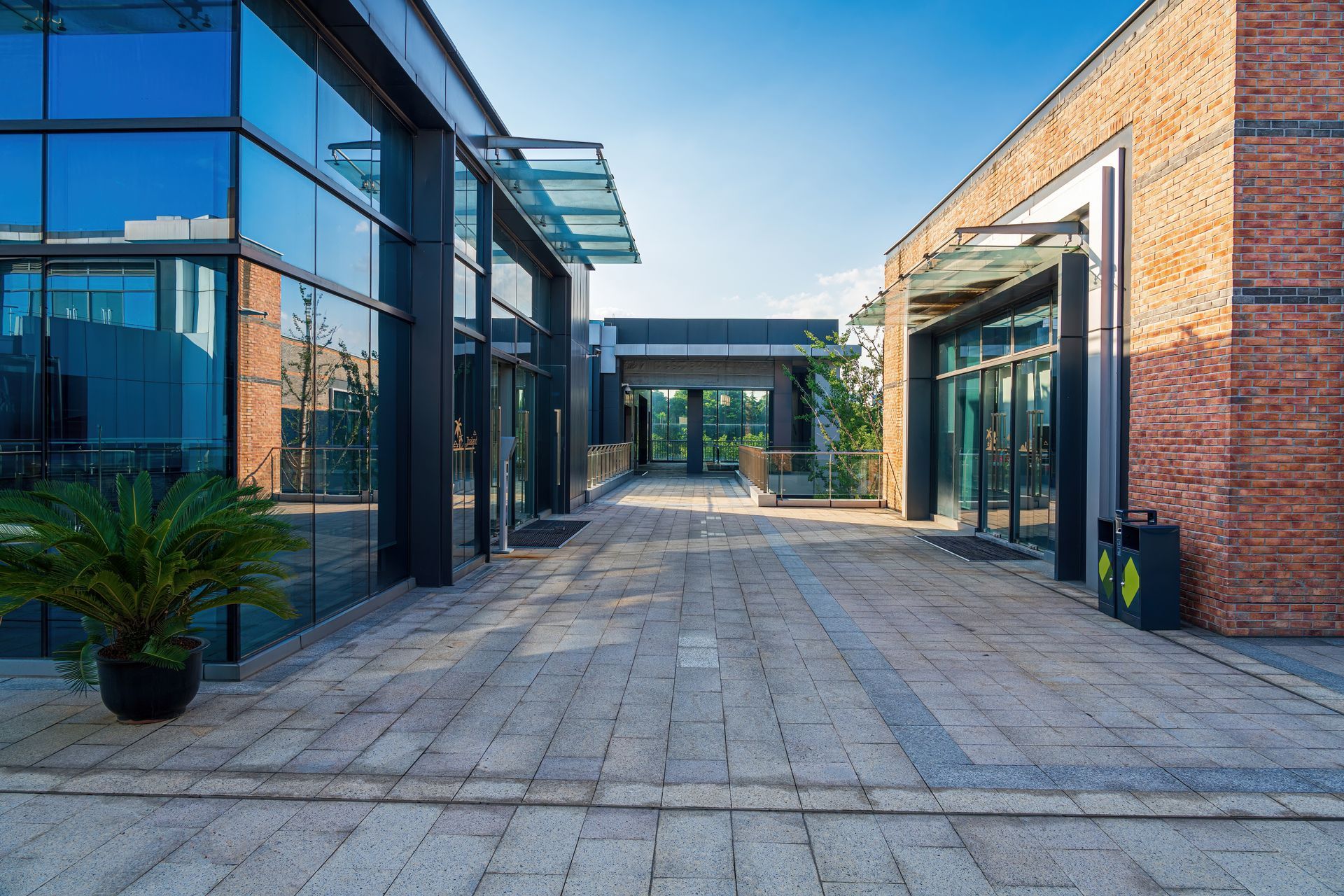 An outdoor paved corridor between modern glass and brick buildings under a clear blue sky.