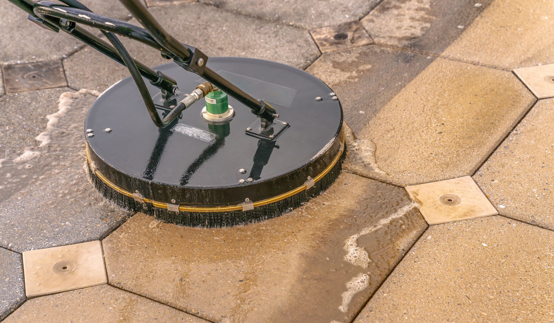 A circular power washer cleaning patterned outdoor pavers, showing clean versus dirty surfaces.