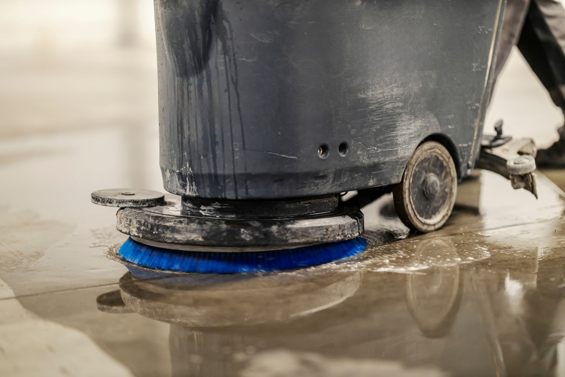 An industrial floor scrubber with a blue brush cleans a wet floor.