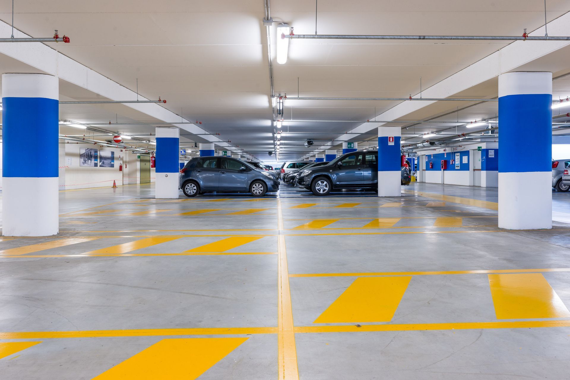 Indoor parking garage with concrete floors, white support columns with blue bands, and yellow painted parking lines.