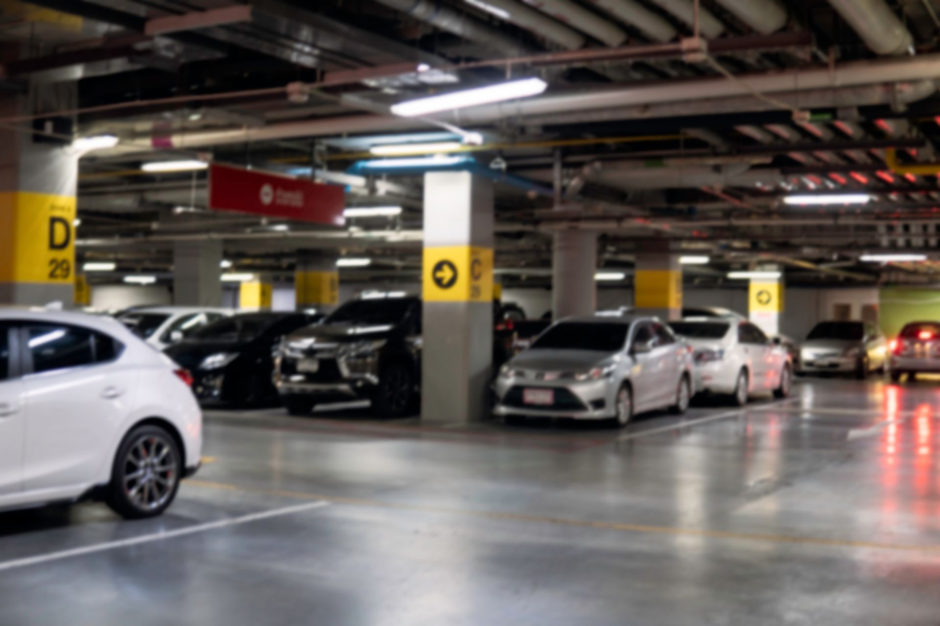 A multi-level indoor parking garage with cars parked in stalls near yellow support pillars marked with letters and arrows.