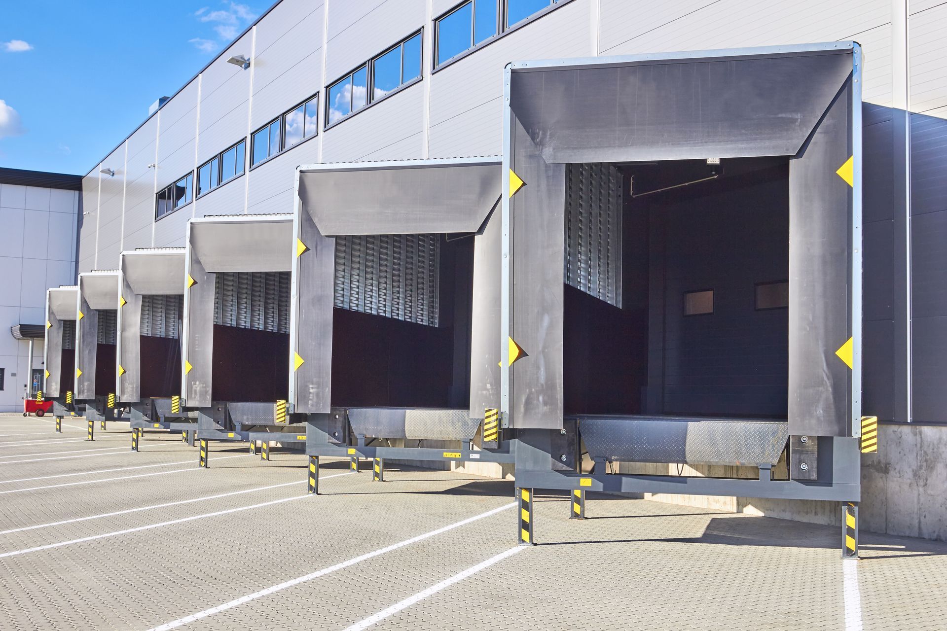 A row of industrial loading docks with black, cushioned shelters attached to the side of a modern white warehouse building.