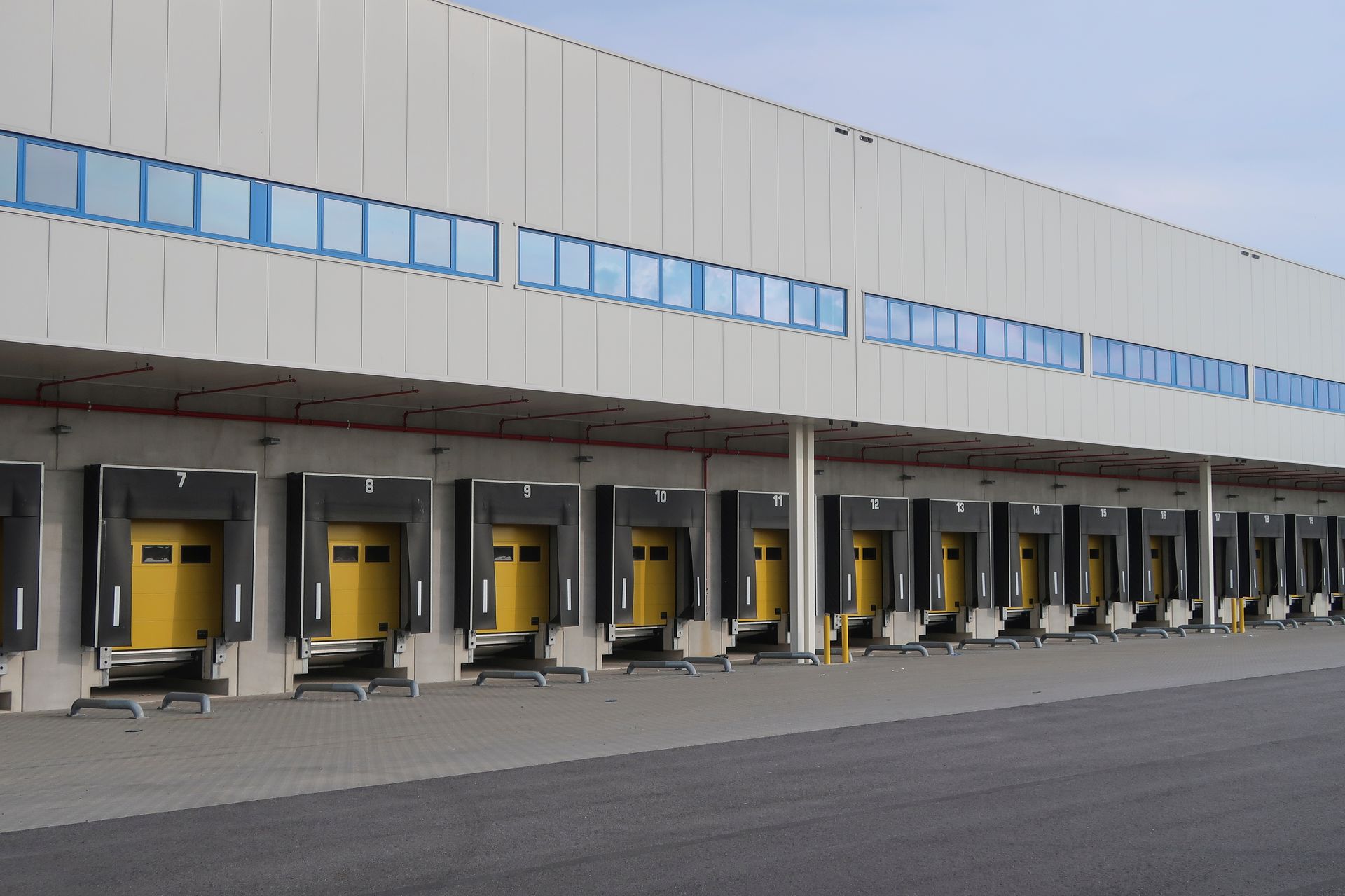 A long industrial warehouse building with a row of many yellow loading dock doors for semi-trucks.