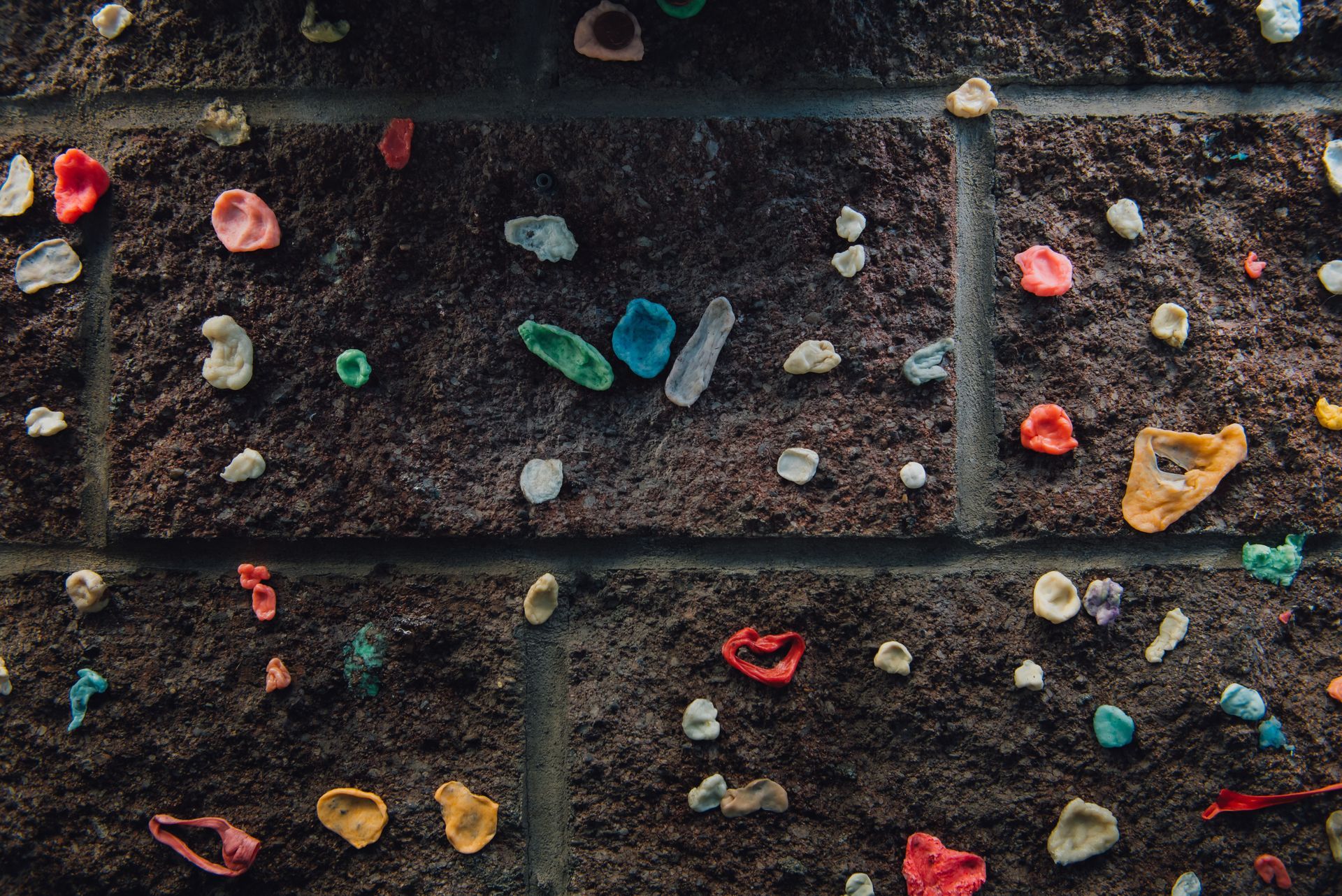 Close-up of a dark brick wall covered in multi-colored pieces of chewed bubblegum.
