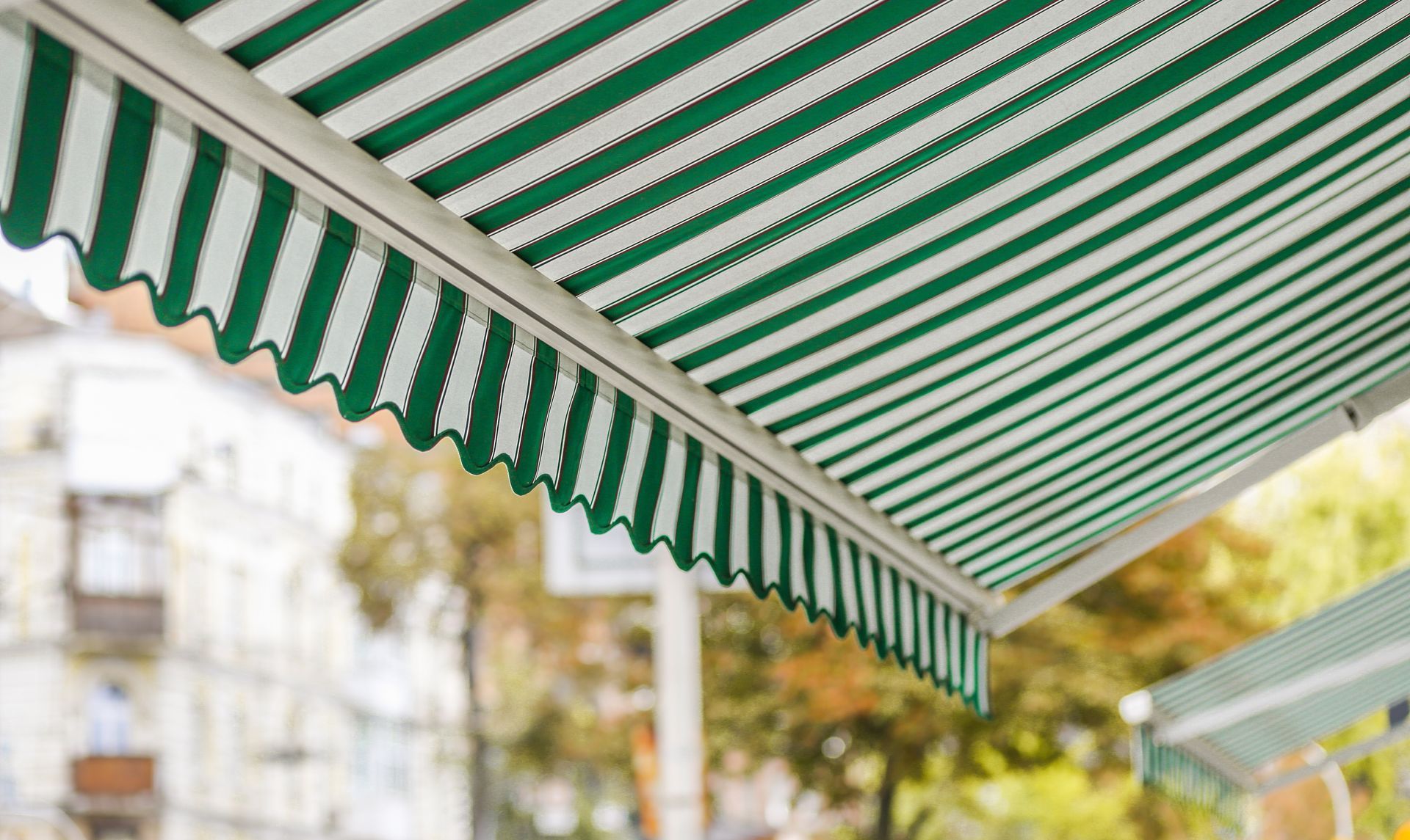 A green and white striped awning extending over an outdoor space, with a blurred urban background.