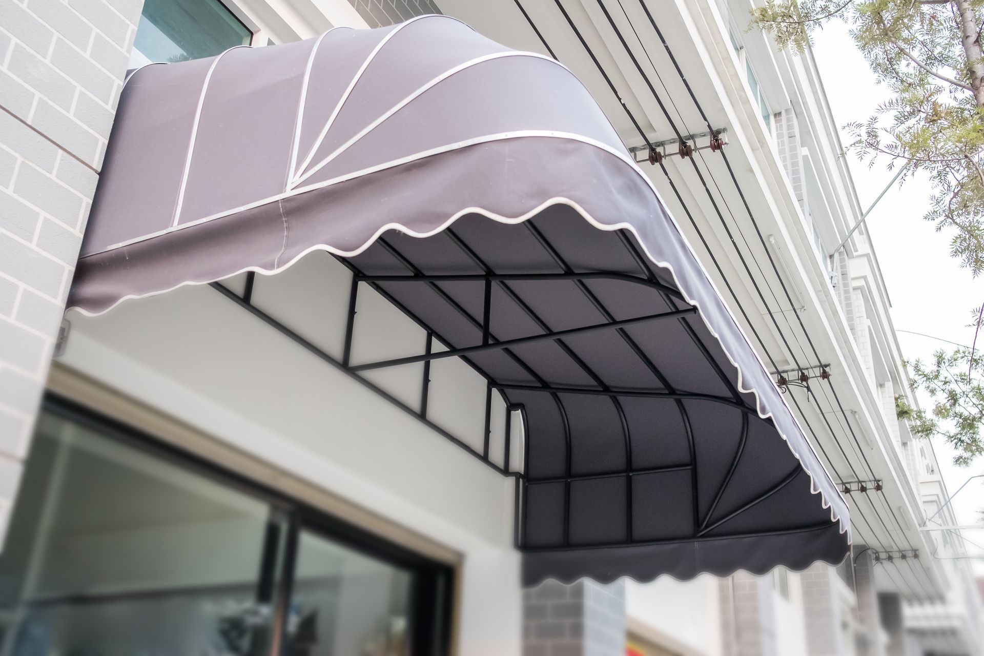 A gray, scalloped fabric awning with white trim mounted above a window on a light-colored building facade.