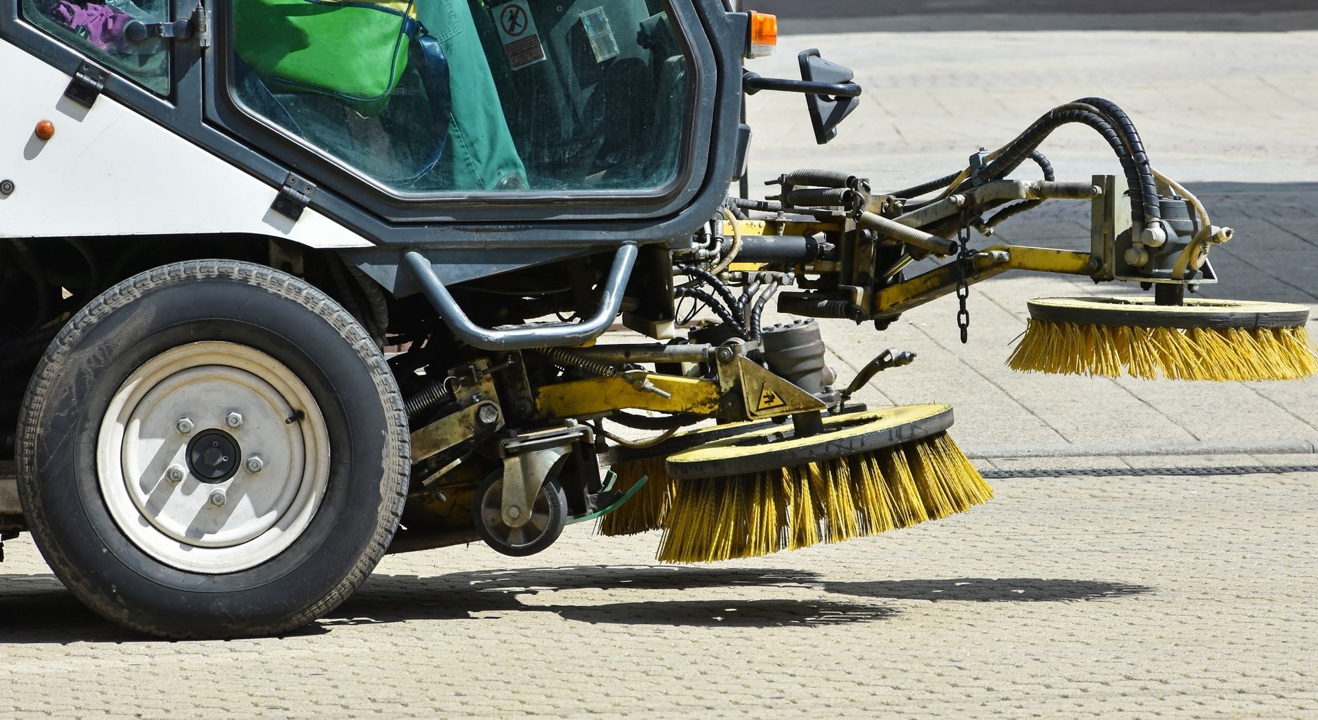 A street sweeper vehicle with two rotating yellow brushes cleaning a paved surface.