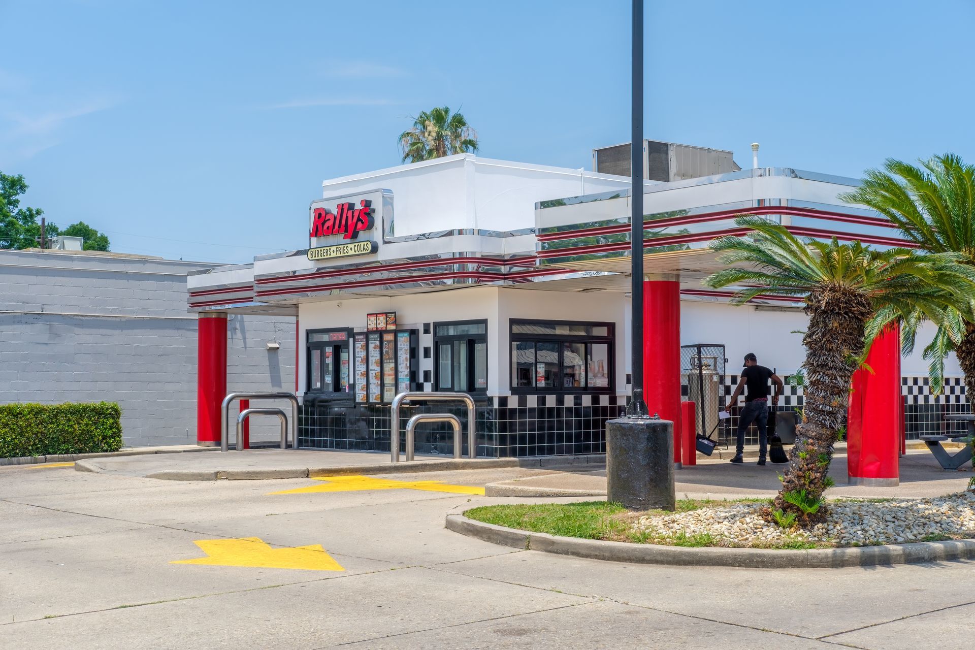 A red-and-white 1950s-style diner building with a drive-thru, parking lot, and a person standing near a red pillar.