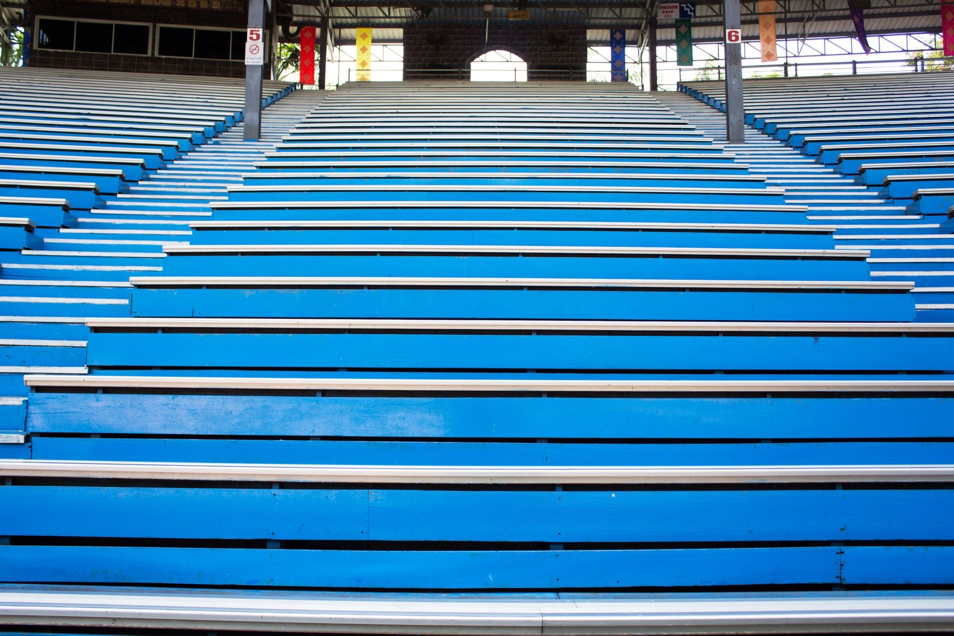Rows of blue stadium seating leading upward toward a covered structure with hanging flags.