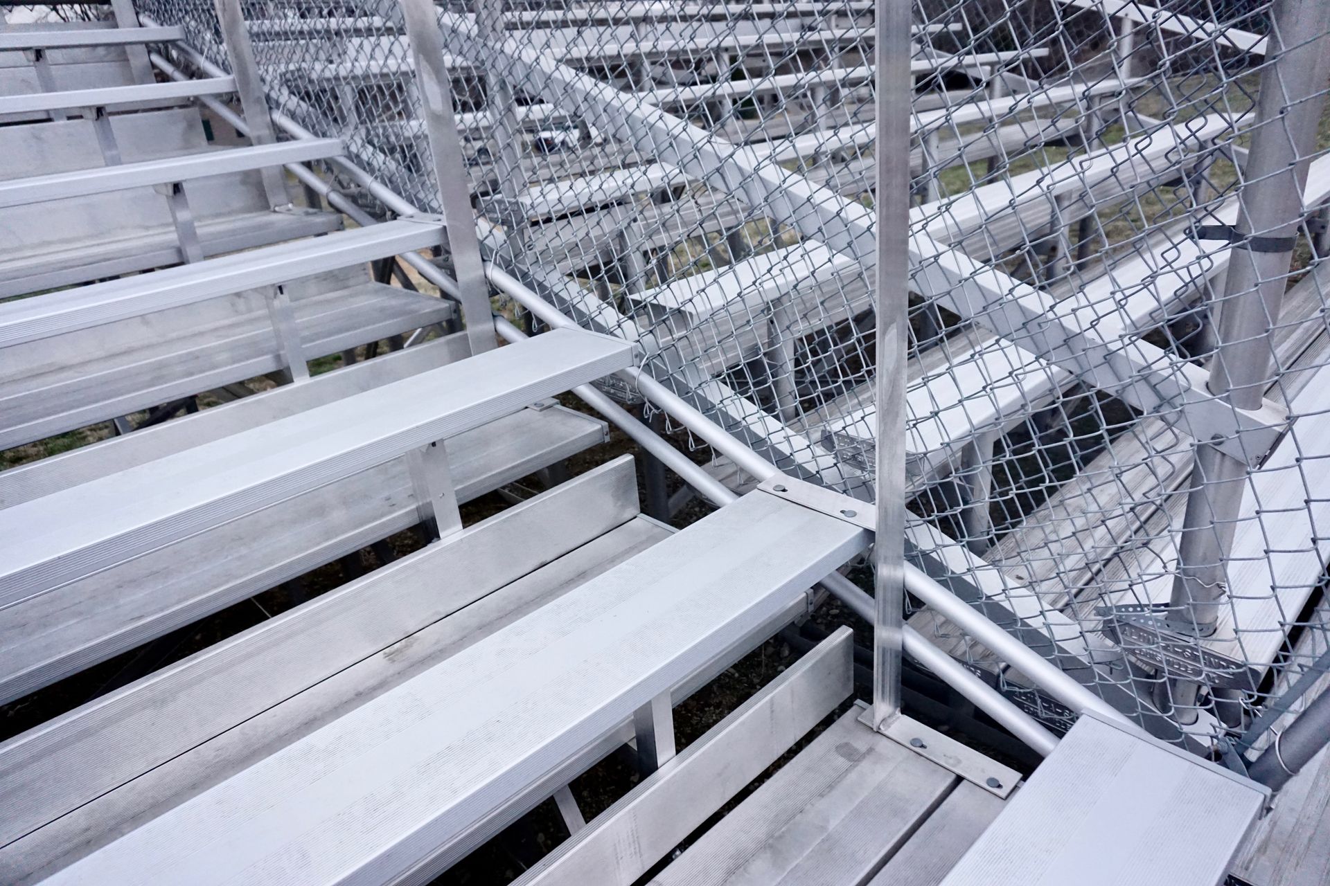 Empty metal bleachers viewed from above, with a chain-link fence separating the rows.