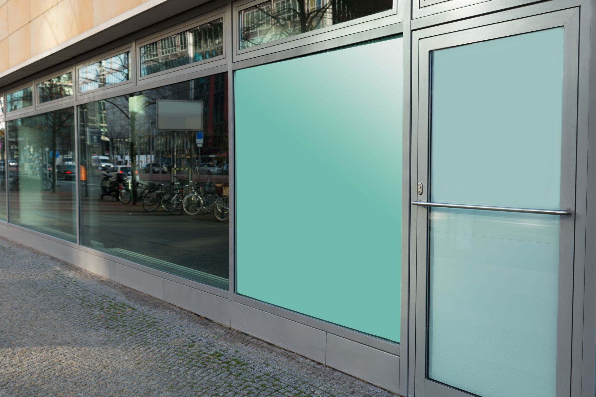 Storefront with a gray metal frame, a glass door, and a large window panel covered in light green privacy film.