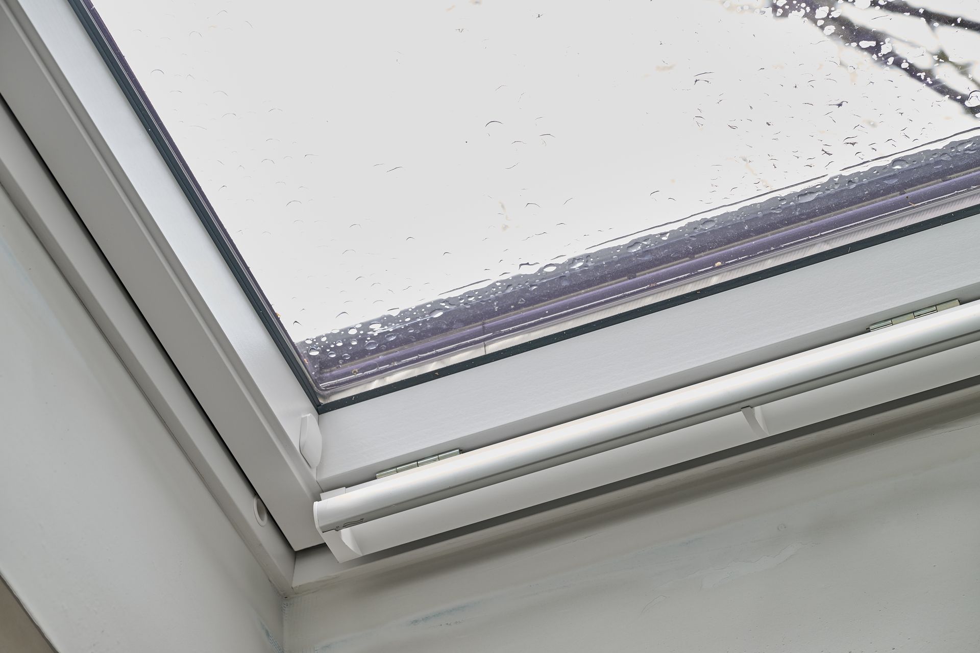 A close-up of a white-framed skylight window with condensation visible on the glass and an attached white trim piece.