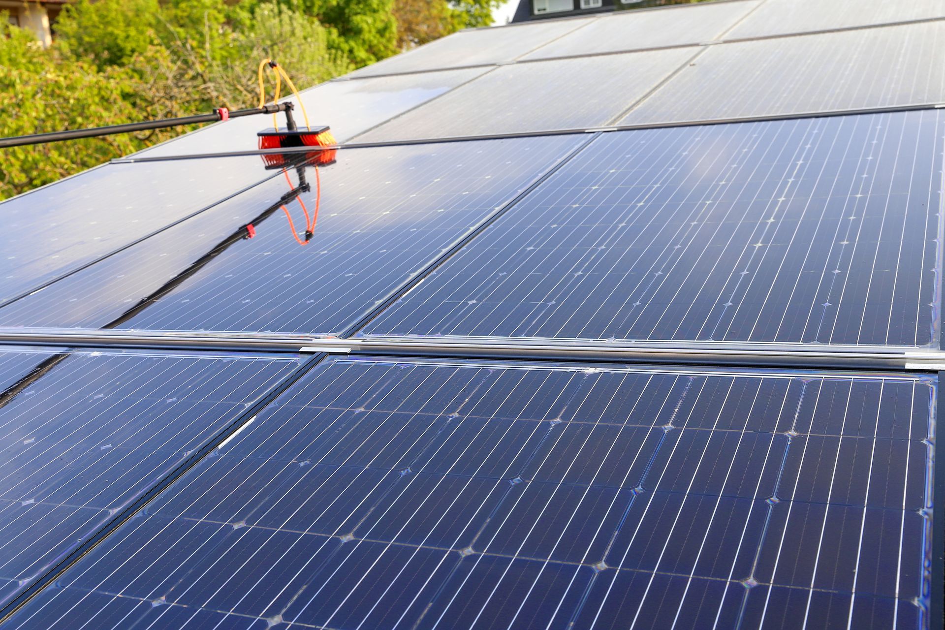 A robotic cleaner moves across dark, grid-patterned solar panels mounted on a roof under a sunny sky.