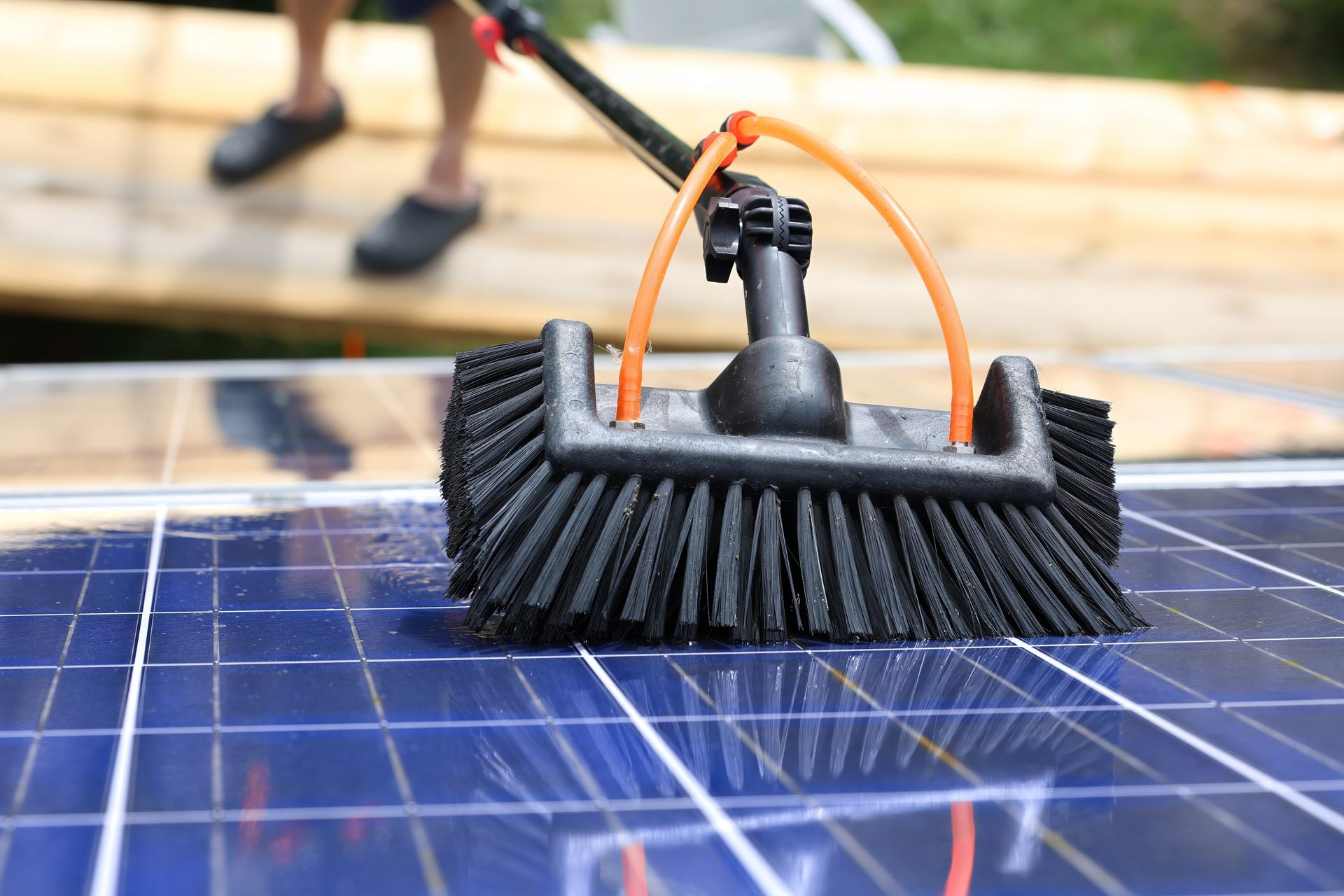 A person using a long-handled brush to clean a solar panel.