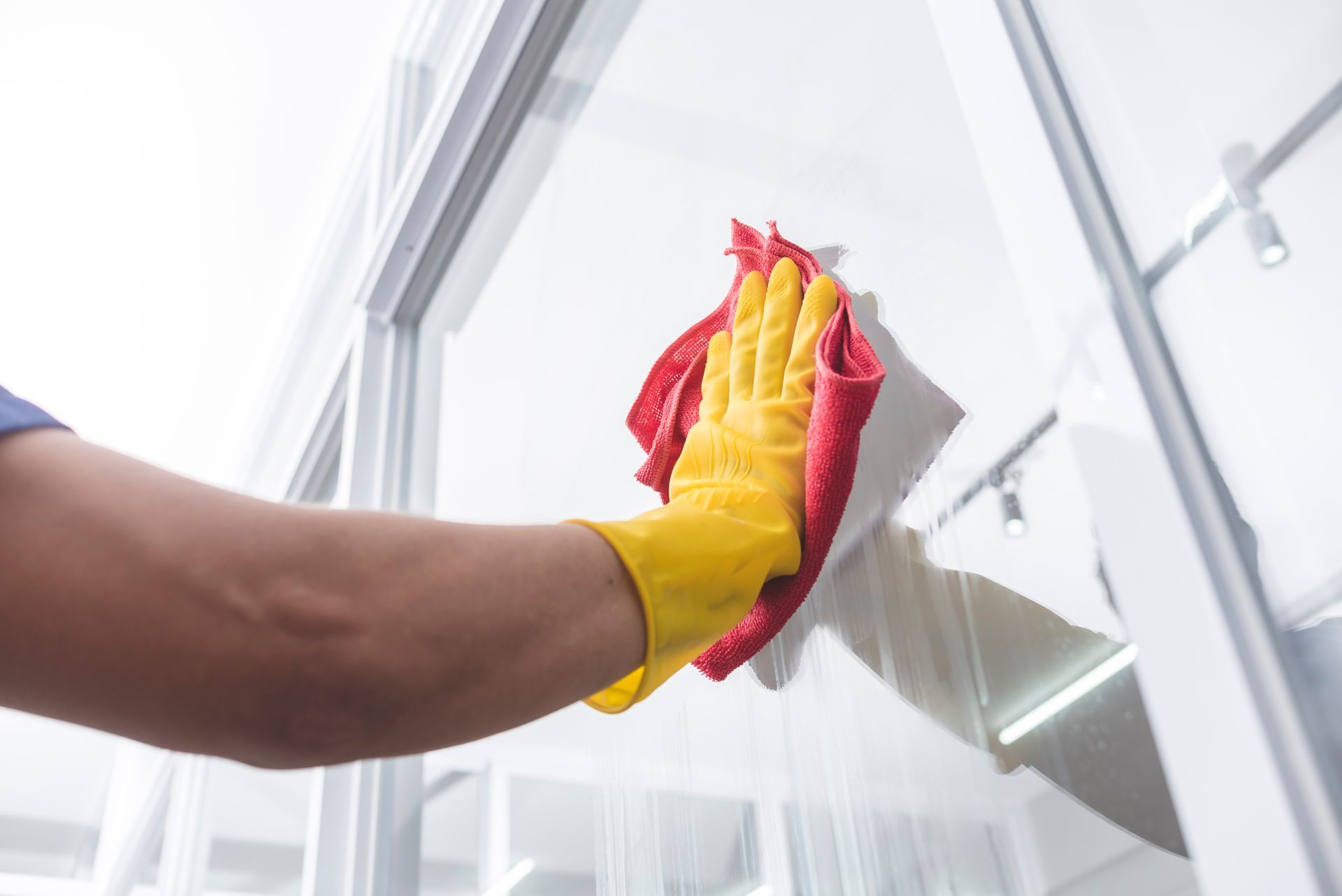 A person wearing a bright yellow rubber glove cleans a white frame surface with a red cloth.