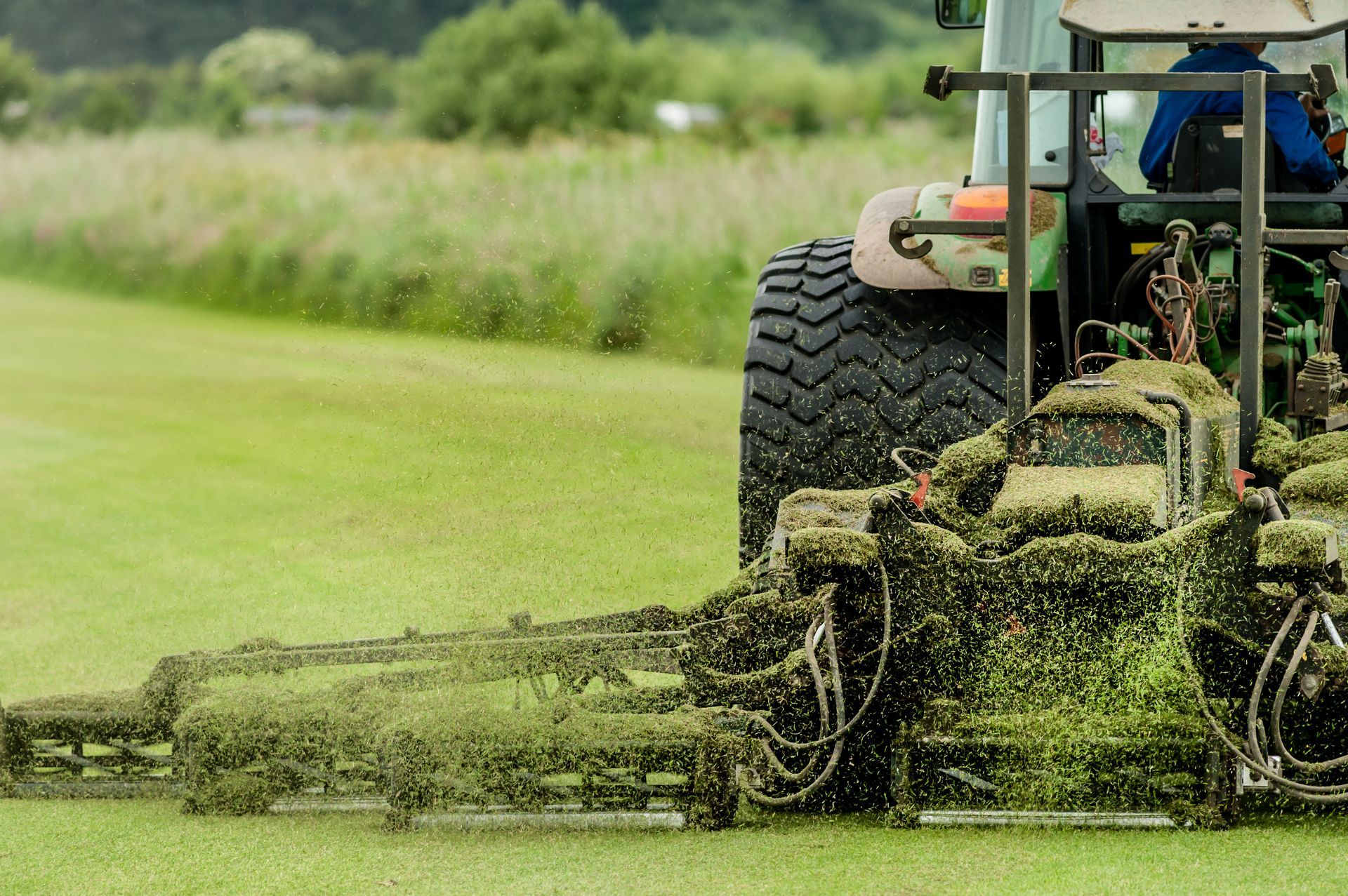 A tractor with a large mower attached cuts a wide swath of grass in a field.
