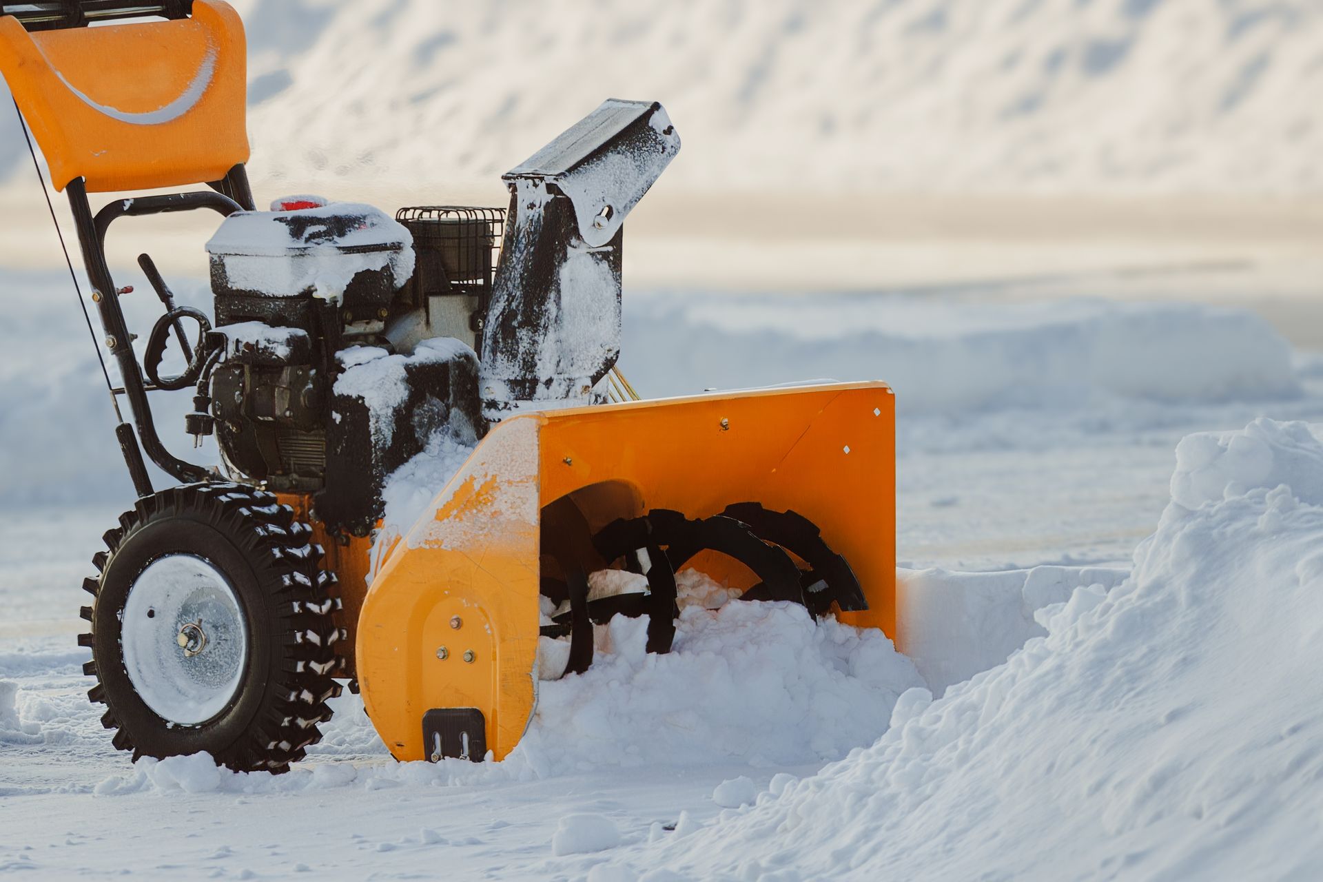 A yellow snow blower clearing a snow-covered path on a bright winter day.