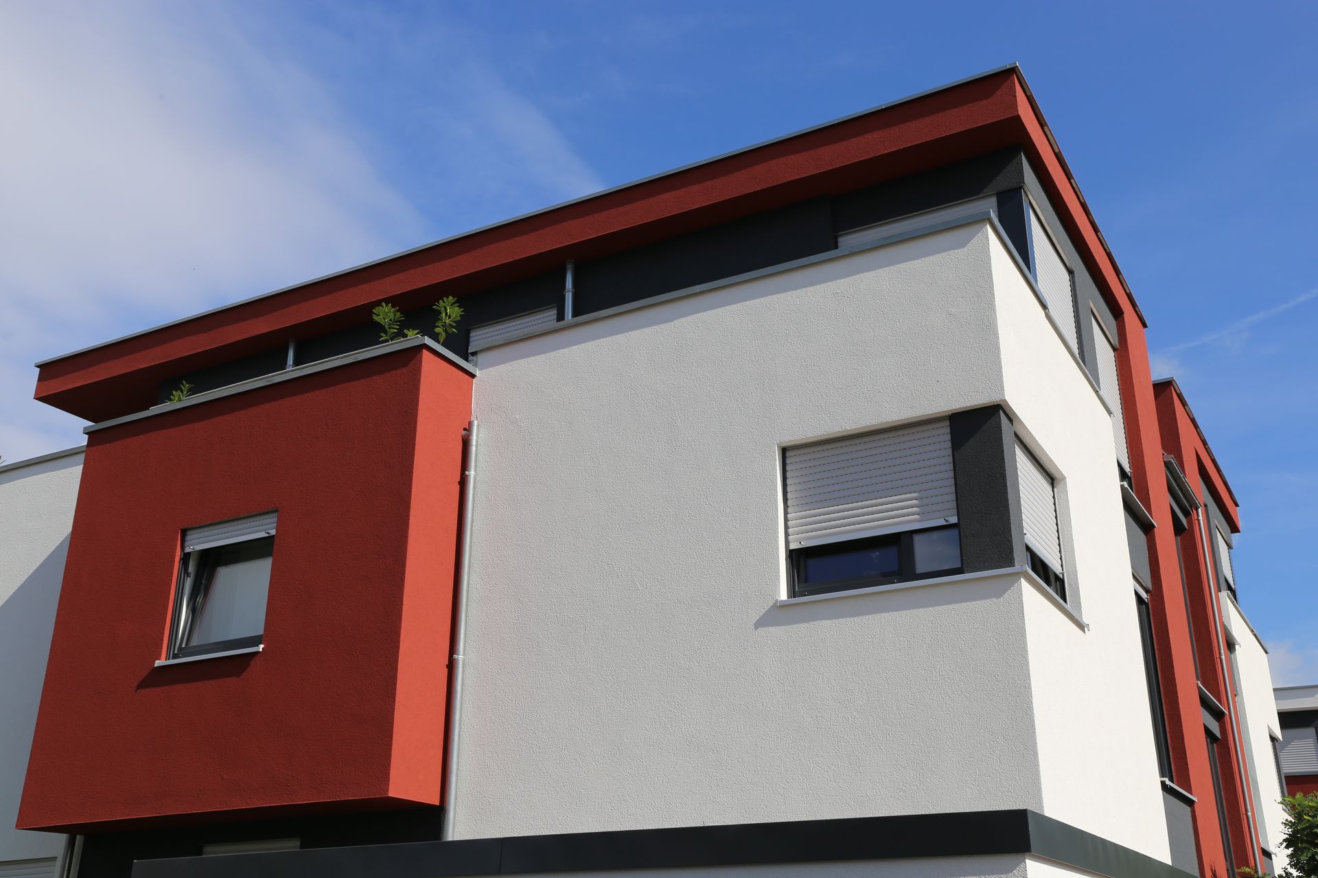 Modern building exterior featuring geometric white and reddish-brown sections against a clear blue sky.