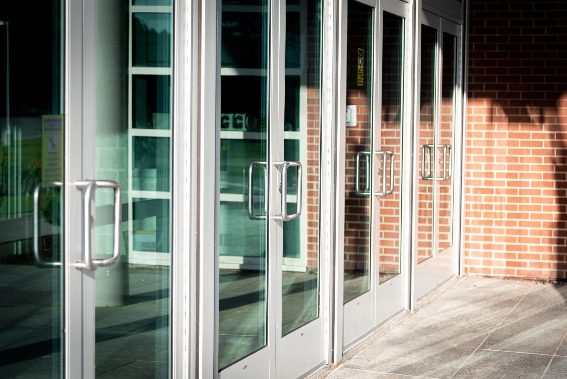 A series of glass entry doors with silver handles and metal frames, set against a red brick building wall.