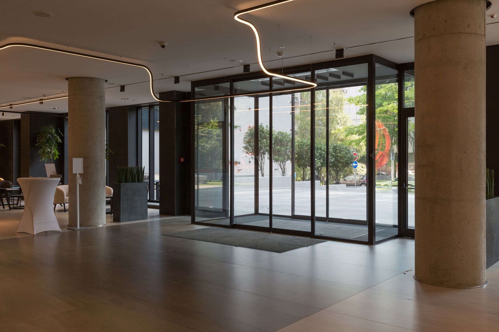 Modern building lobby with a central glass entryway, polished tile floors, and a circular concrete structural column.