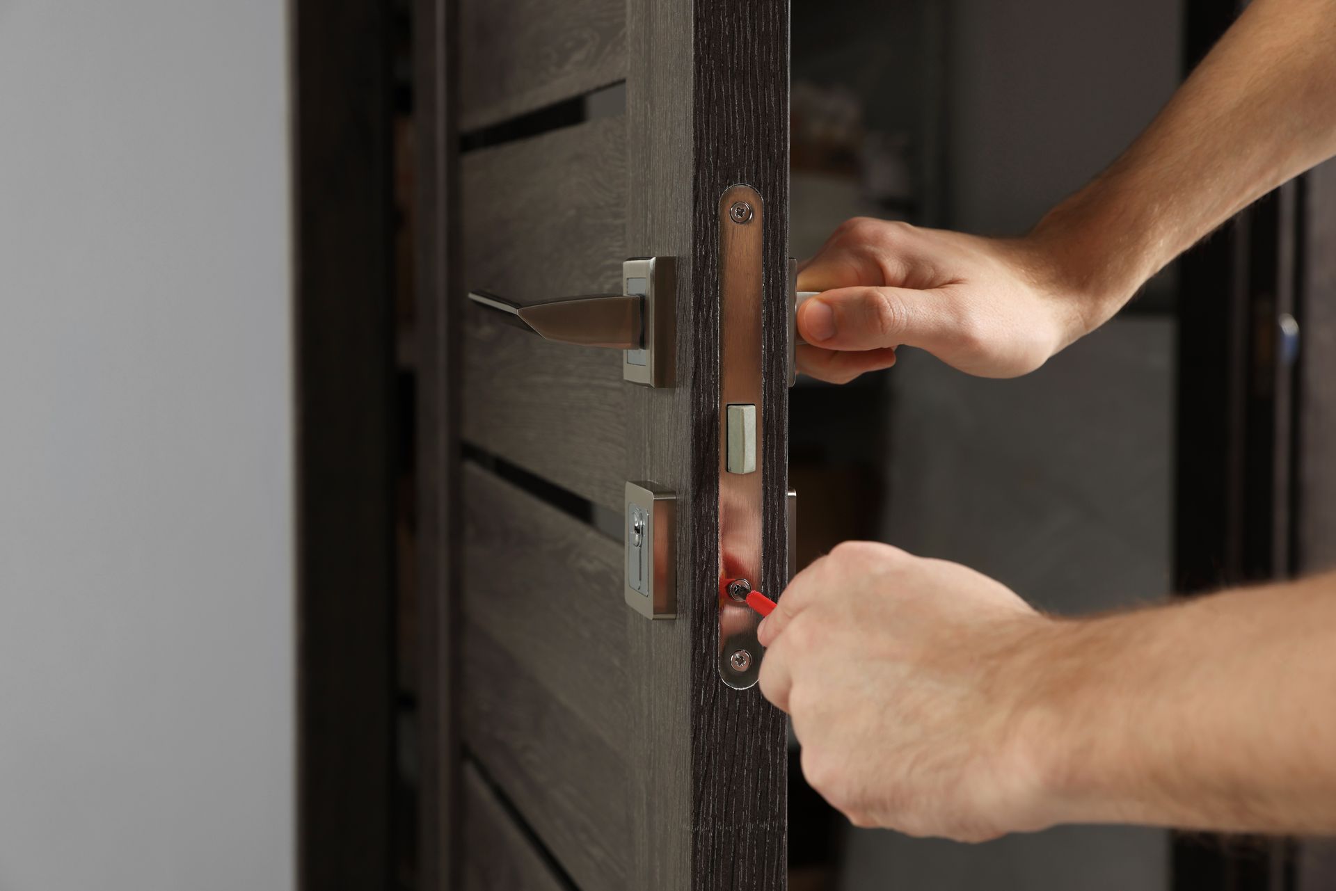 Hands inserting a key into a door lock on a dark wooden door with modern hardware.