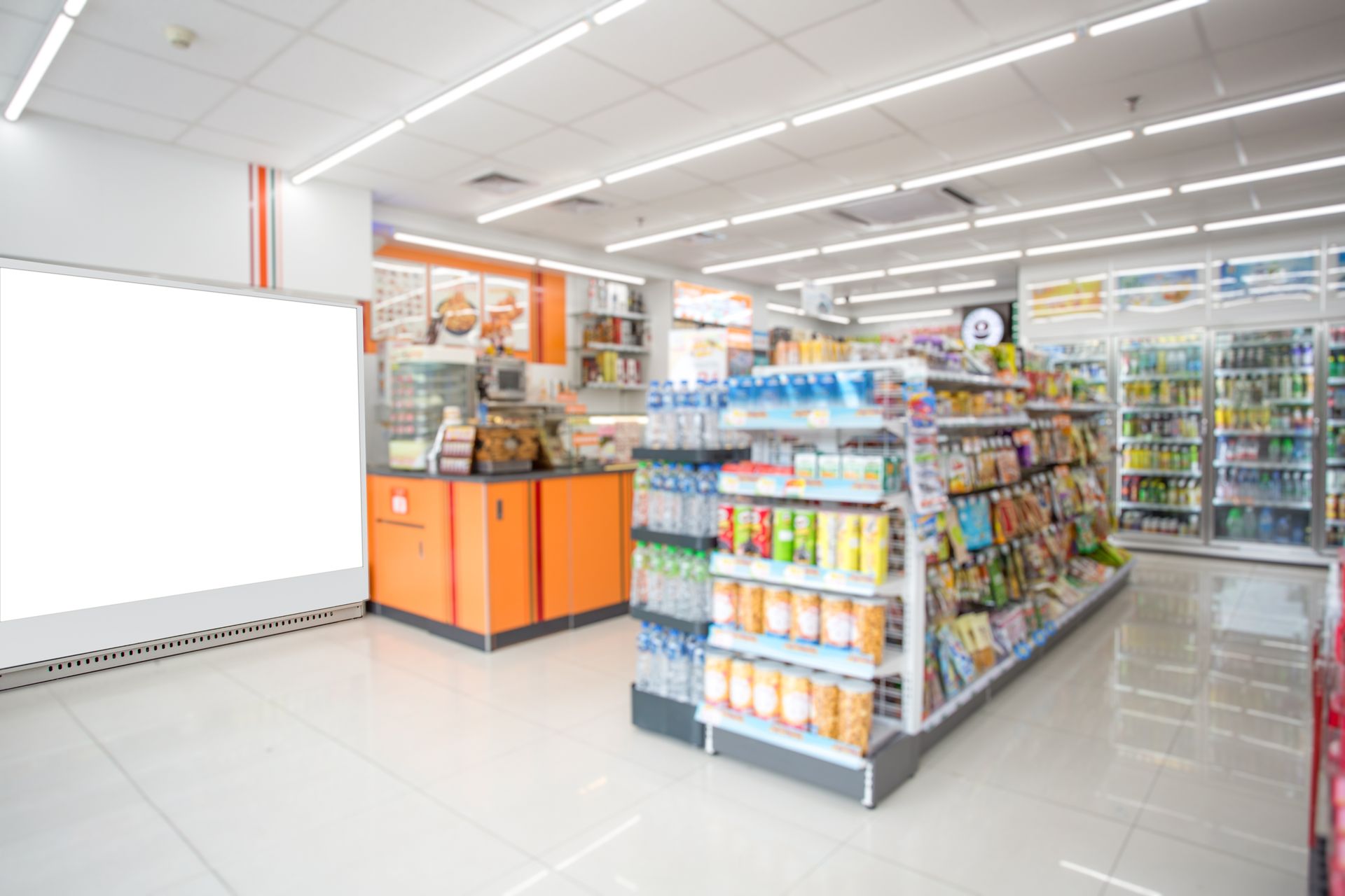 A bright, modern convenience store interior featuring orange checkout counters, tall stocked shelves, and refrigerated cases.