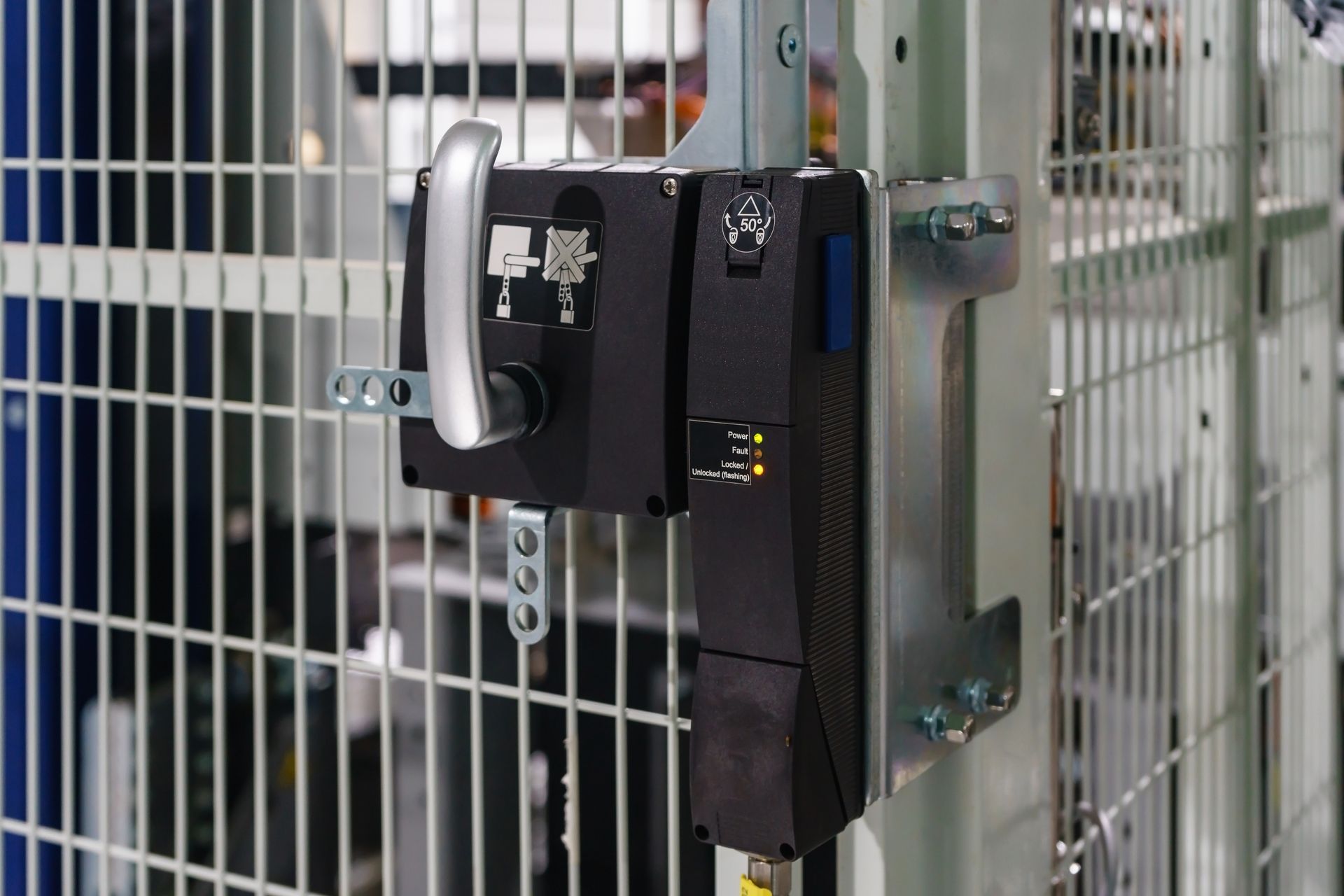 An industrial safety interlock switch mounted on a metal wire mesh guard, featuring a handle and illuminated status lights.