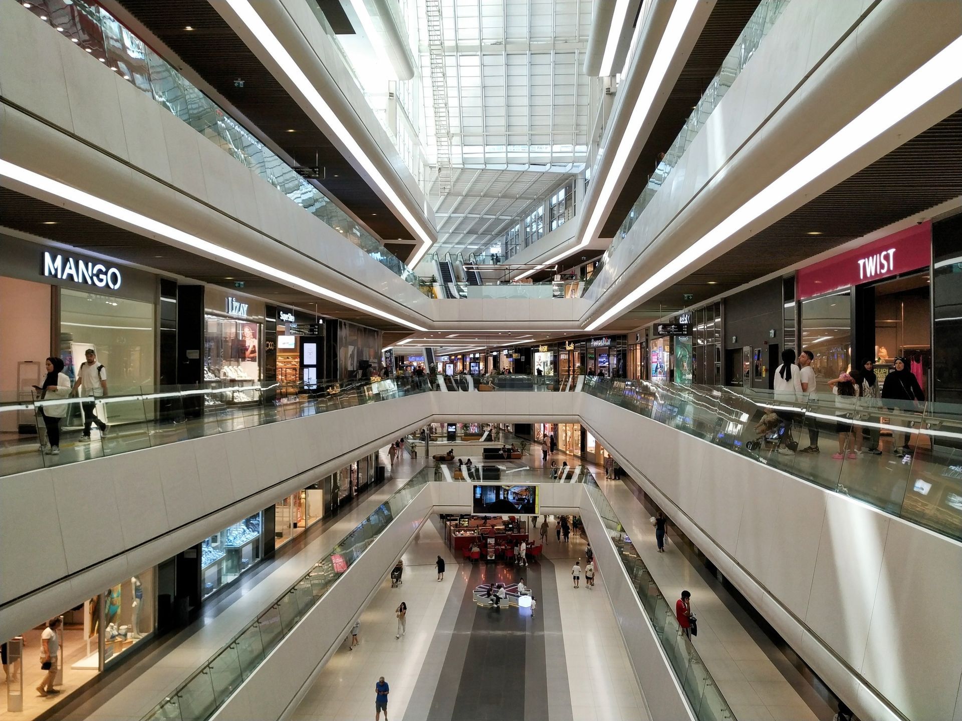 A view of a modern, multi-level shopping mall with glass railings, bright interior lighting, and storefronts.