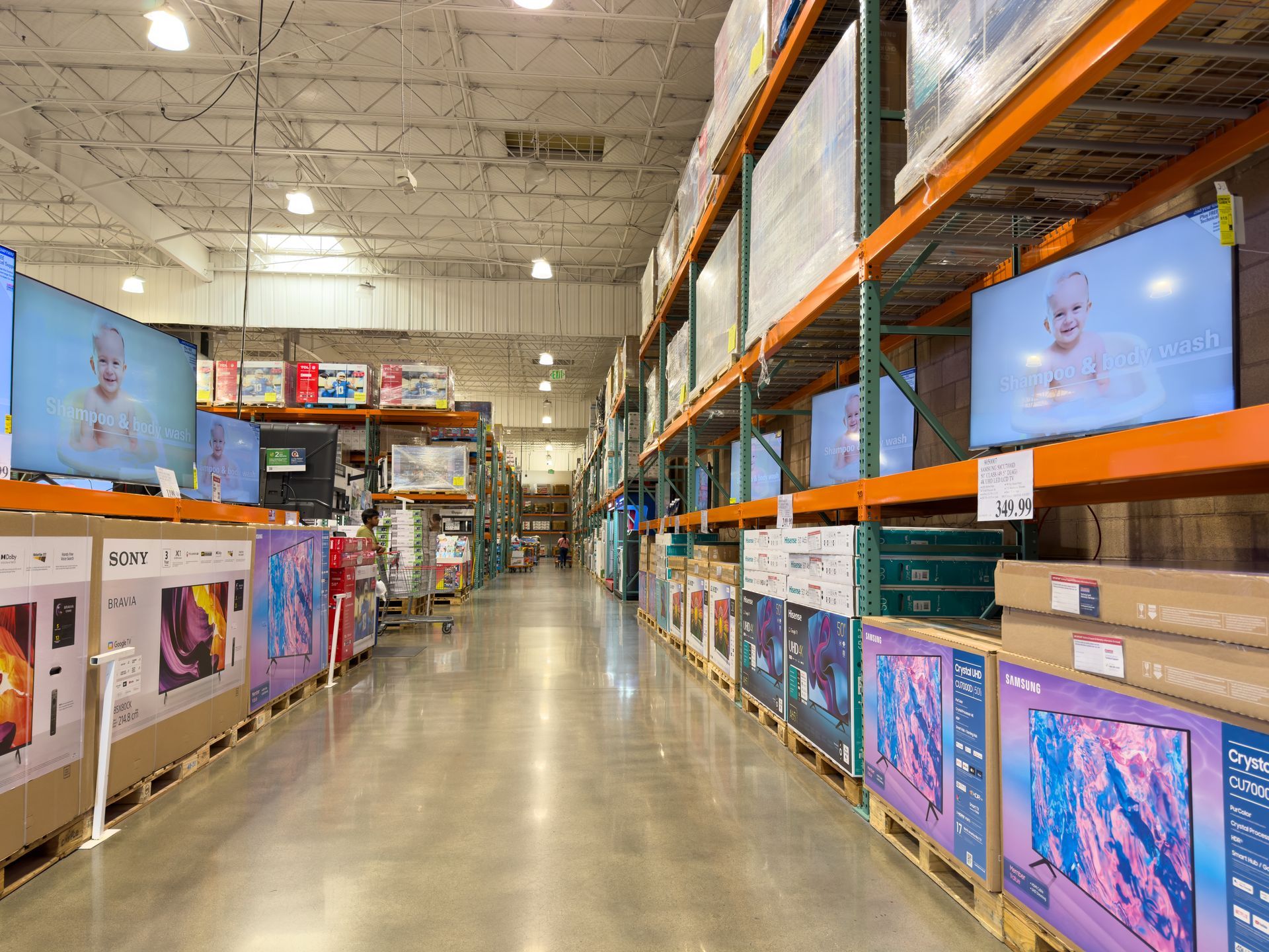 A warehouse store aisle filled with large flat-screen televisions displayed on metal shelving units.