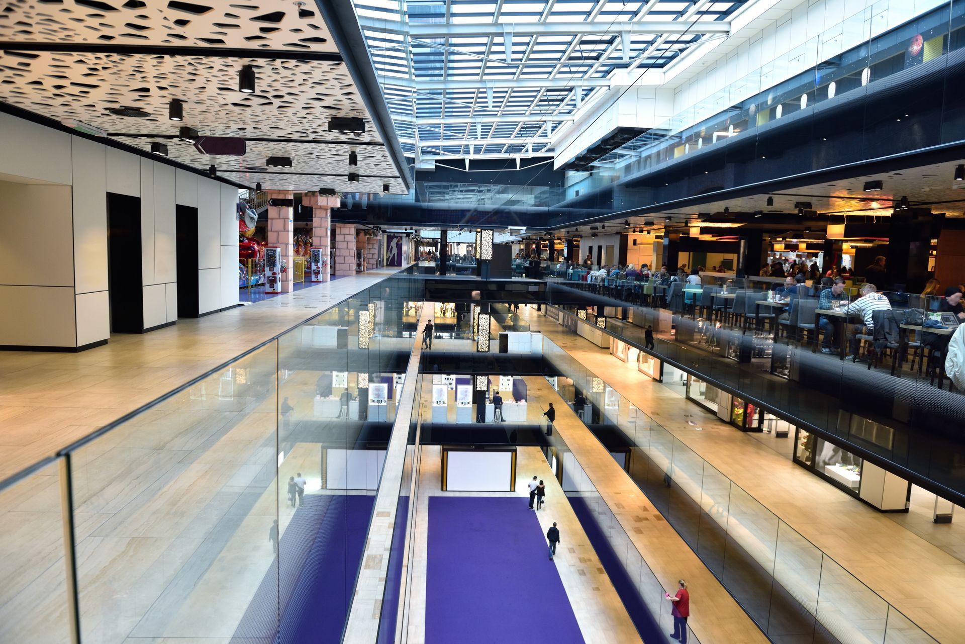 An interior view of a multi-level shopping mall with a central atrium, glass railings, and modern architecture.