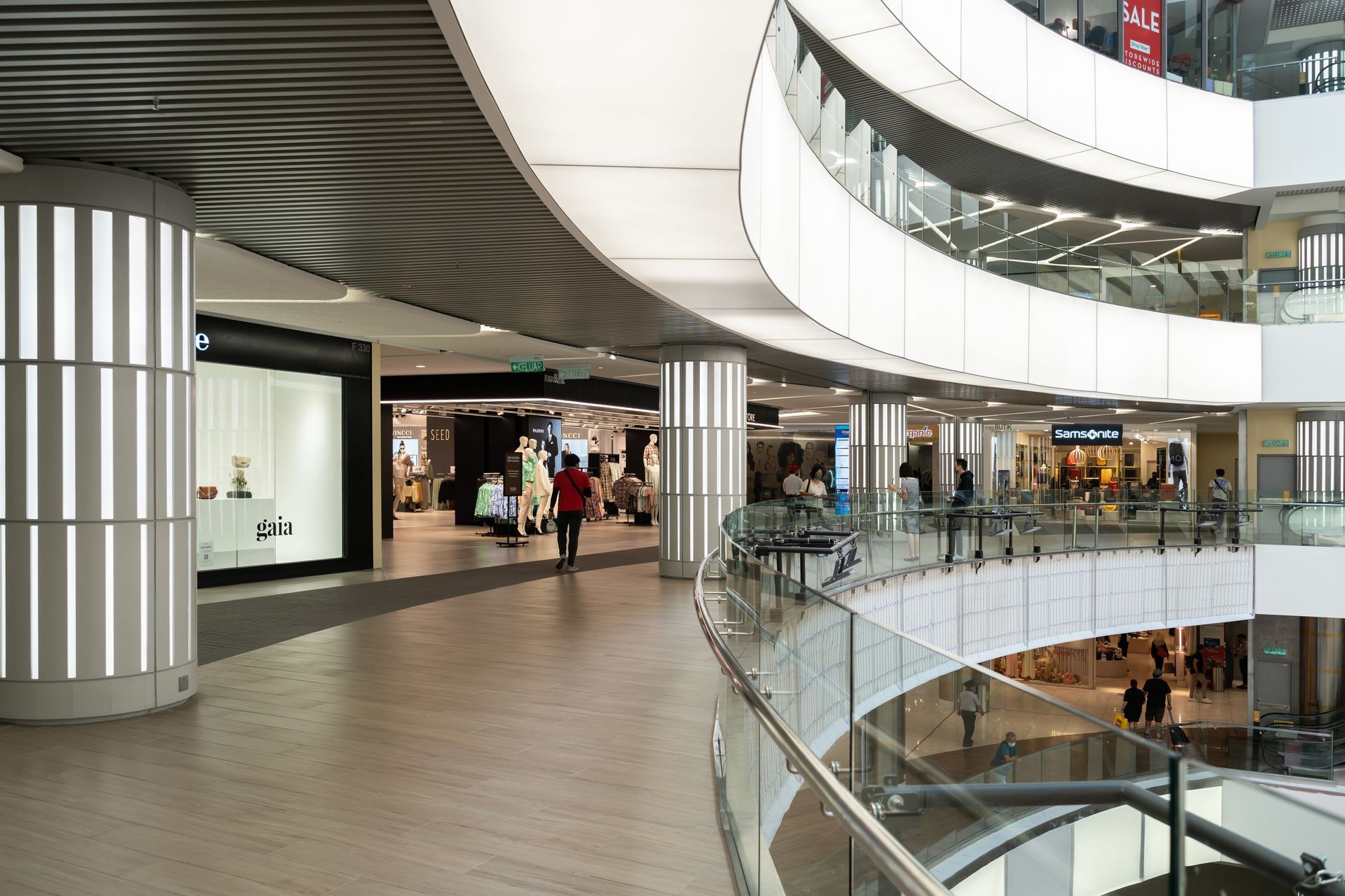 A modern, multi-level shopping mall interior with polished floors, glass railings, and brightly lit retail storefronts.