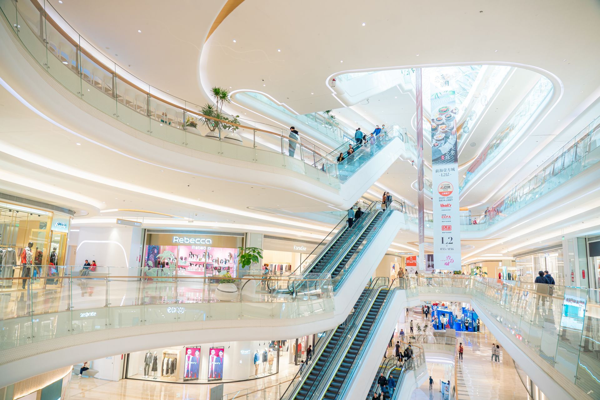 A multi-level shopping mall with white curved balconies, large skylights, and escalators connecting the different floors.