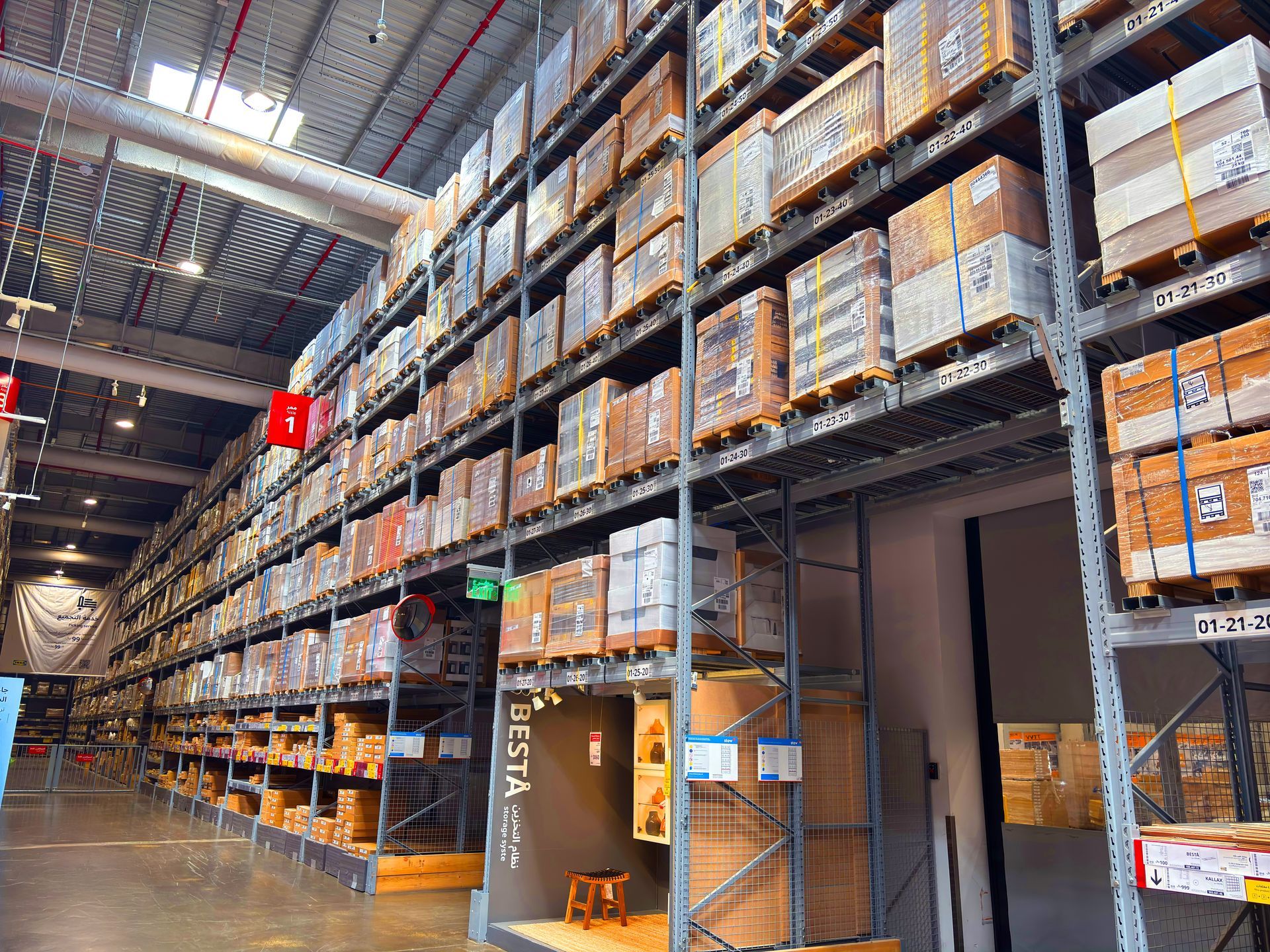 A large warehouse featuring towering metal shelves filled with stacked cardboard boxes and pallets.
