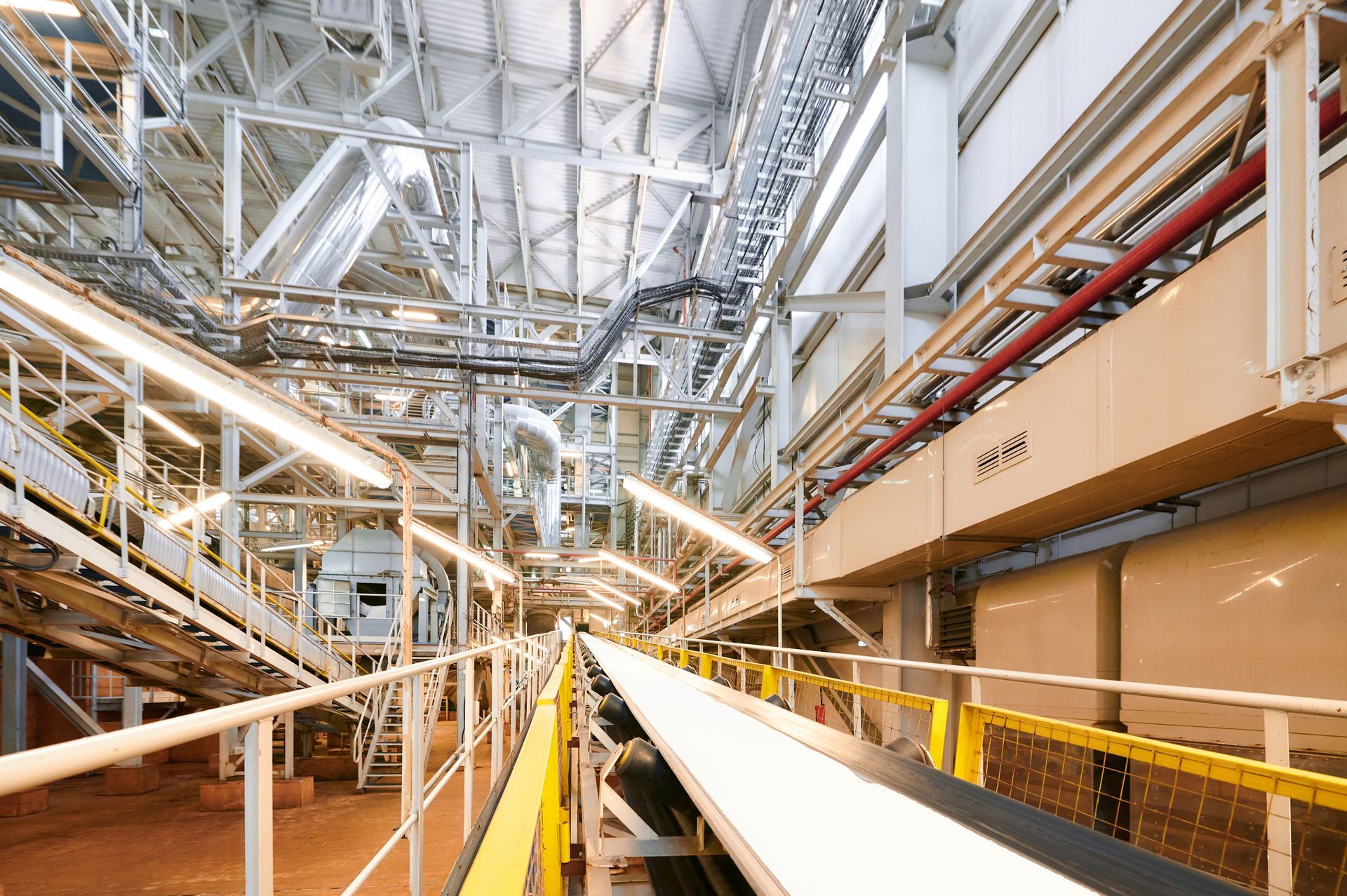 An industrial plant interior features a long conveyor belt running through a large, multi-level metal structure.