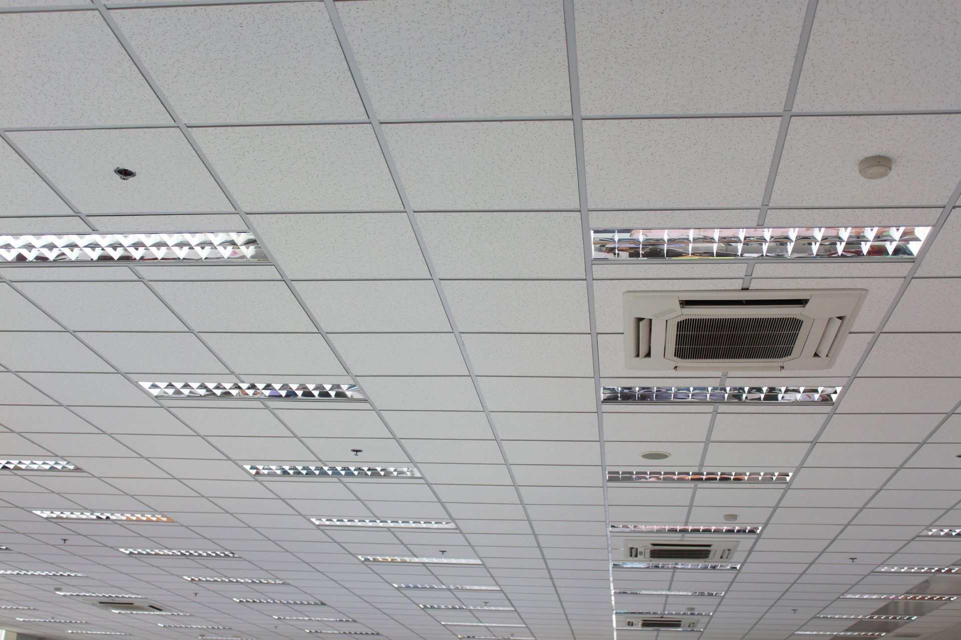 A drop ceiling grid featuring inset fluorescent light fixtures and HVAC vents.