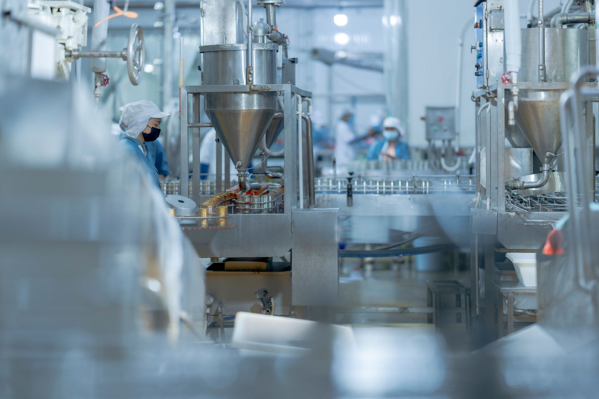 Workers in protective gear operate an industrial liquid filling machine on a factory assembly line.