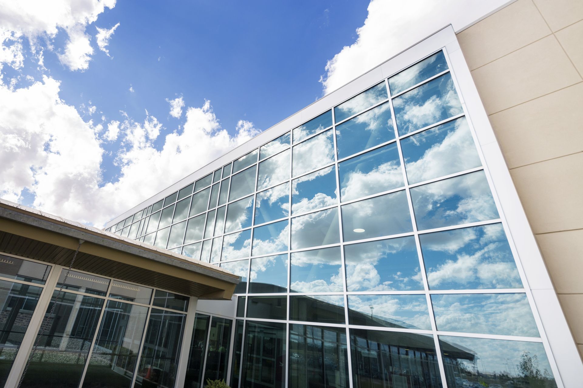 A modern building with a large glass facade reflecting a bright blue sky with white clouds.