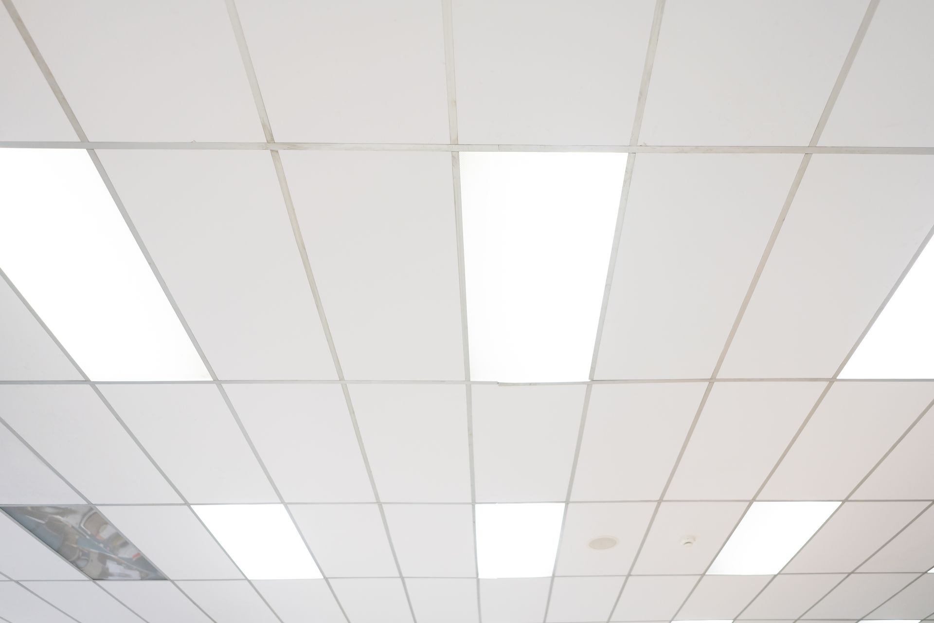 A drop ceiling with a grid of white tiles and several rectangular, bright LED light panels.