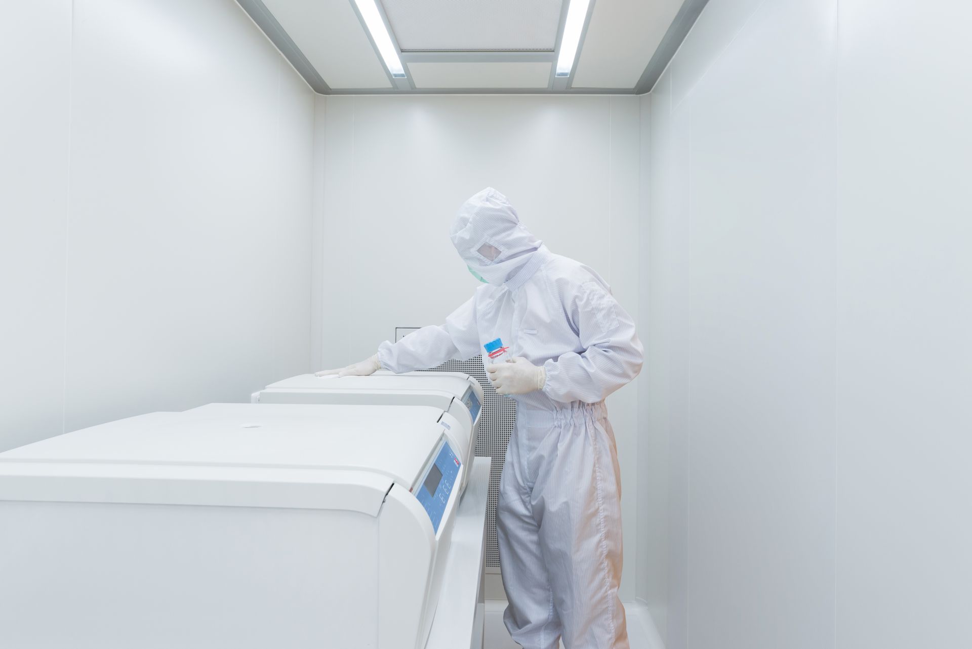 A person in white protective gear works with laboratory equipment in a sterile, white room.