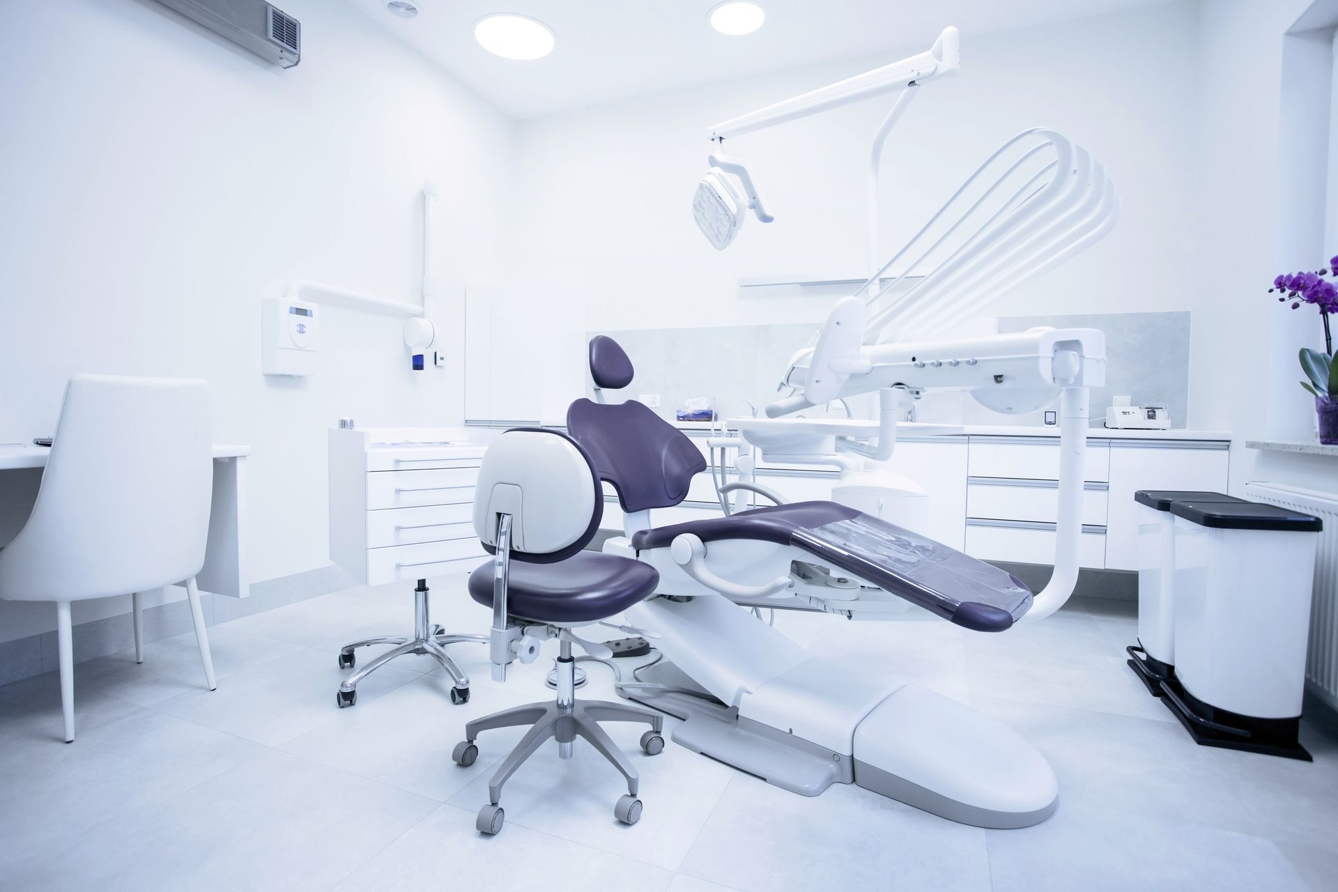 A modern, minimalist dental office with a white dental chair, medical stools, equipment, and a bright, clinical aesthetic.