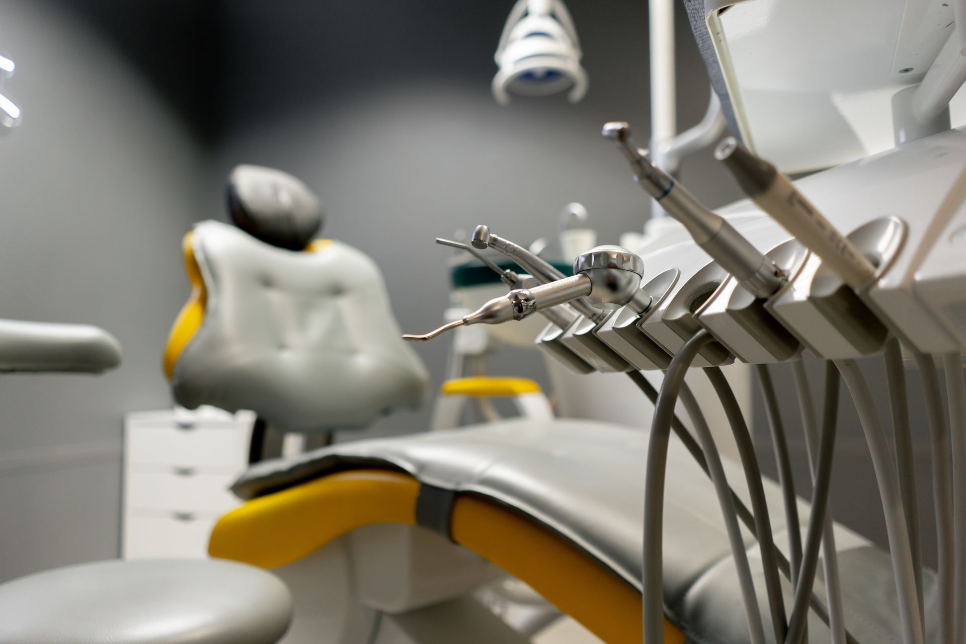 A blurry dental chair with a yellow seat and a sharp focus on metallic dental tools in the foreground.