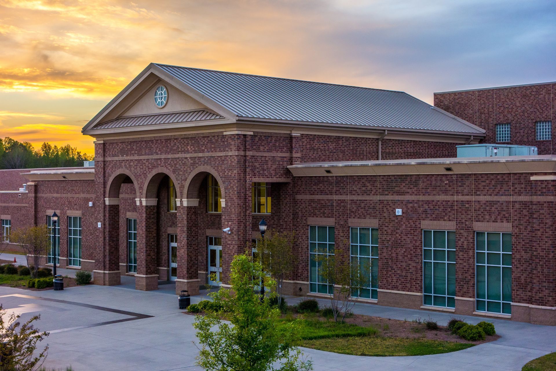 A multi-story brick school building with a columned front entryway under a golden sunset sky.
