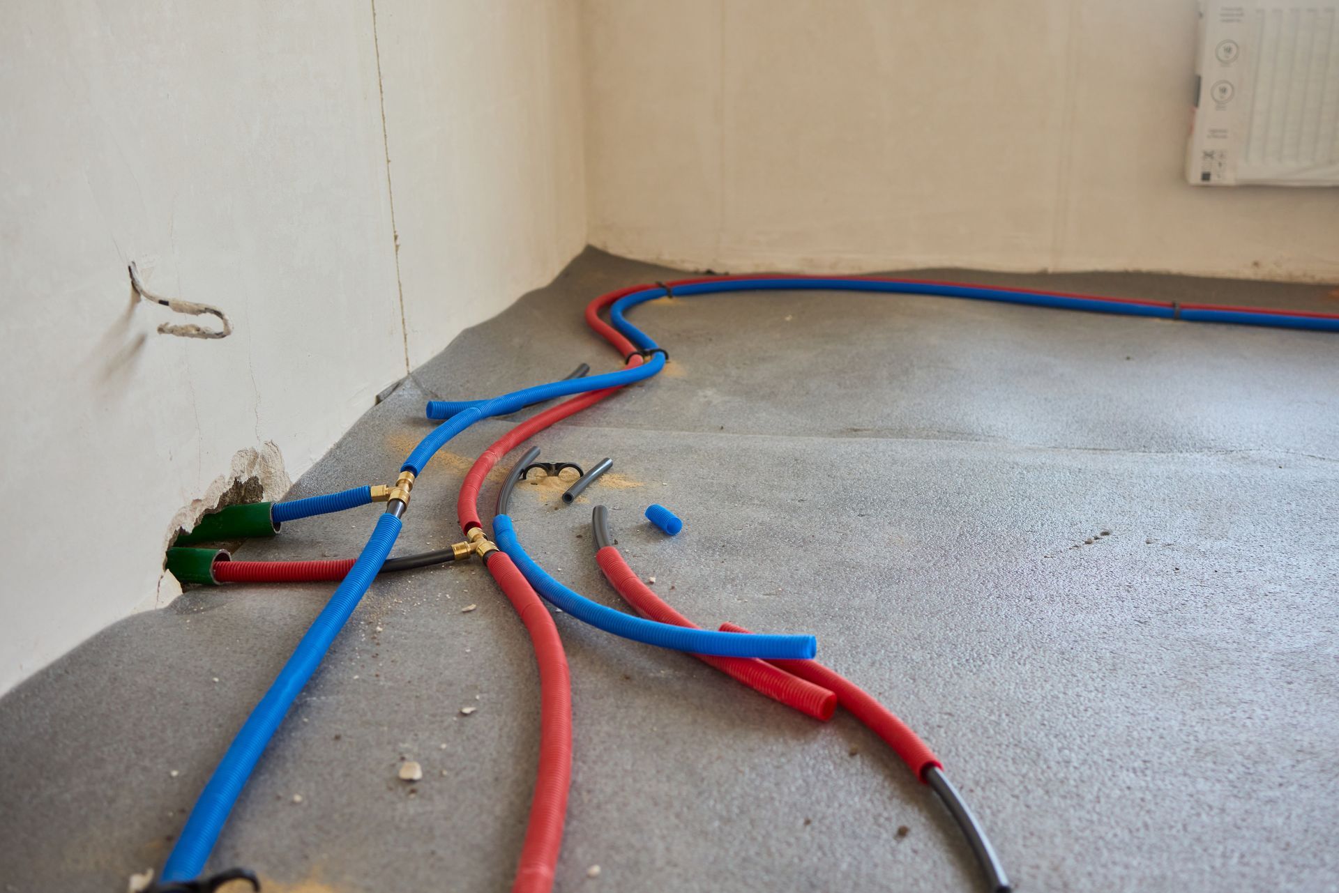 Red and blue flexible plumbing pipes installed across a concrete floor in a room under renovation.